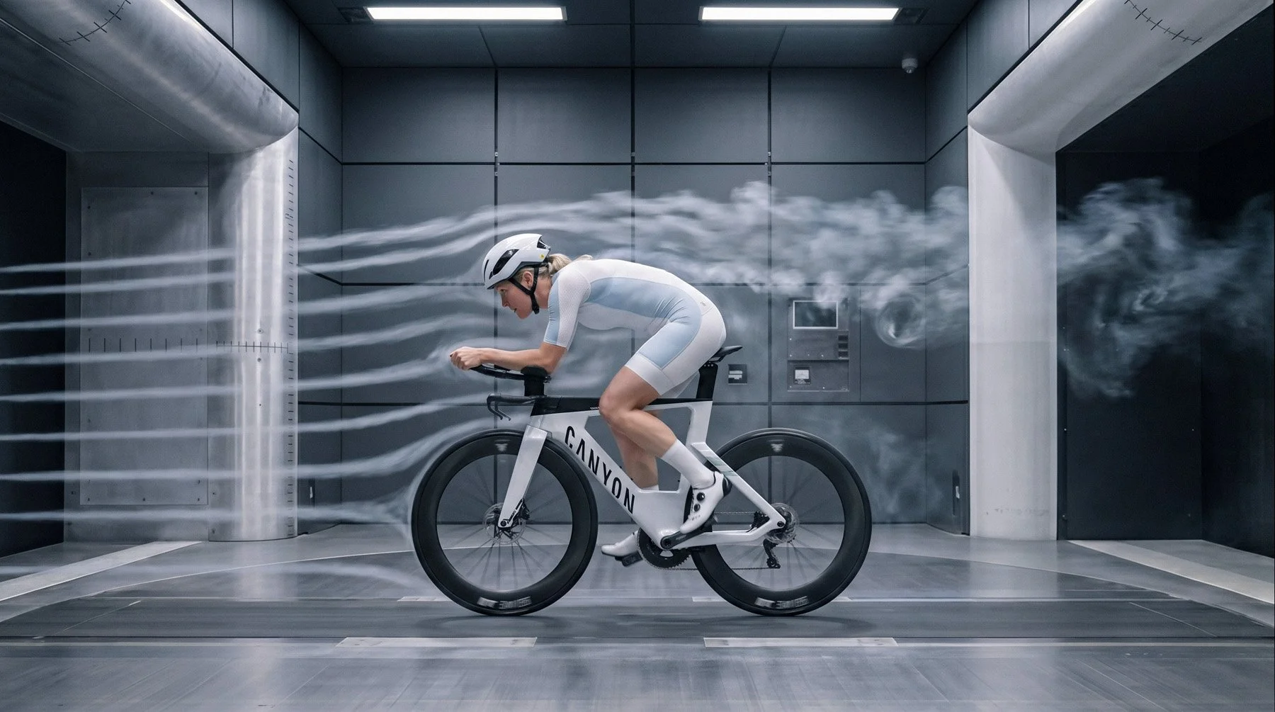 A person in athletic gear and a helmet riding a futuristic CANYON-branded bicycle in a high-tech, elevator-like room with dark gray walls. The scene has a digital effect with white streaks resembling wind or motion lines, giving a sense of speed.