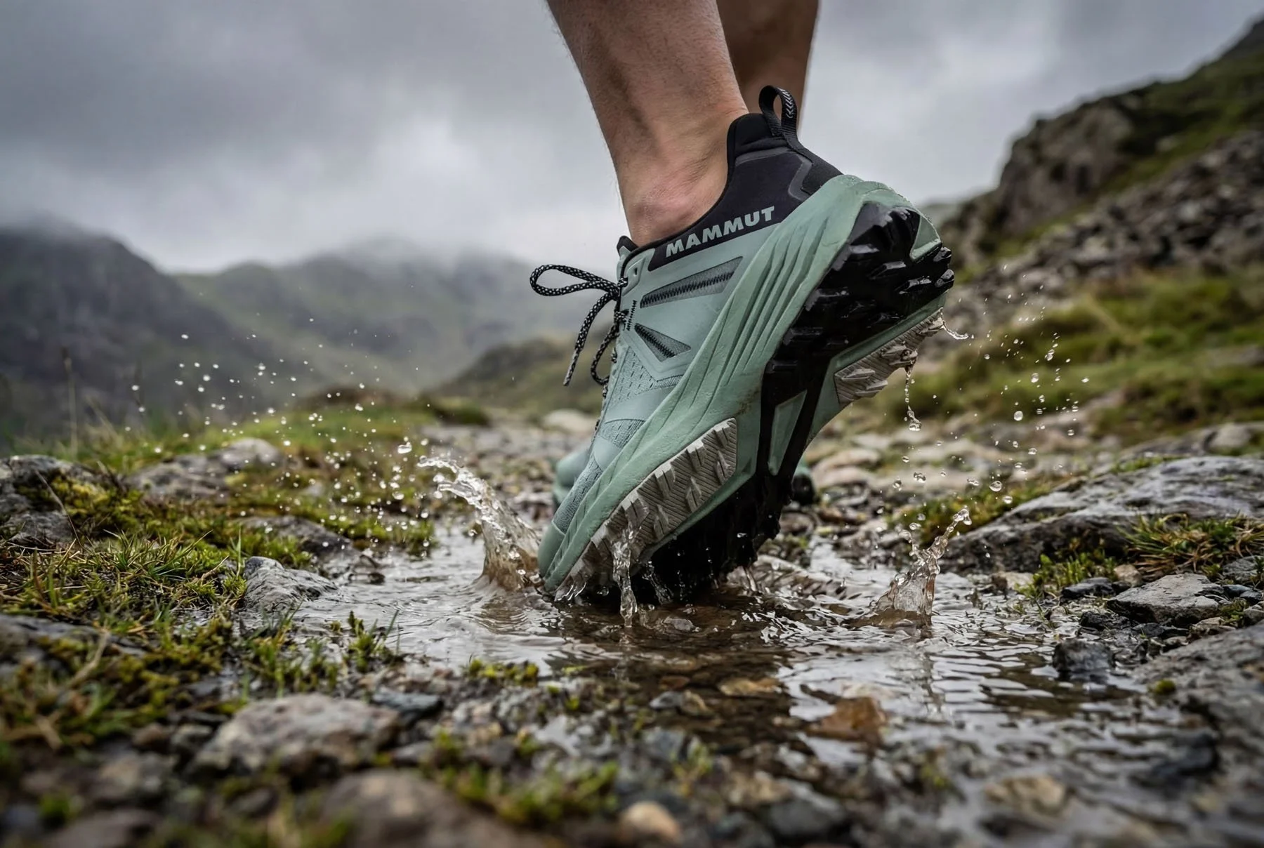 Close-up of a person wearing hiking shoes crossing a rocky wet stream in a mountainous outdoor landscape.