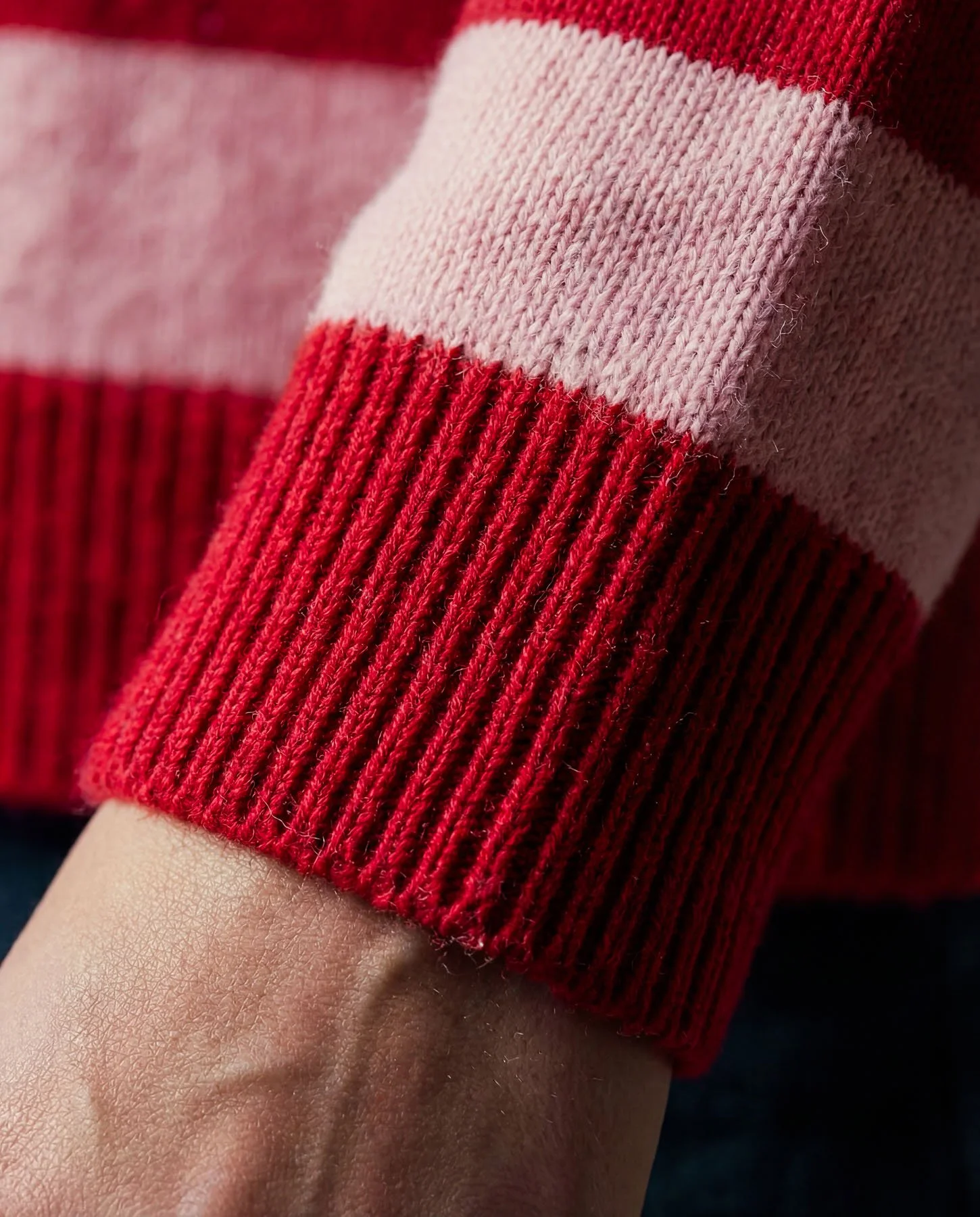 Close-up of a red and pink striped sweater sleeve with ribbed cuff.