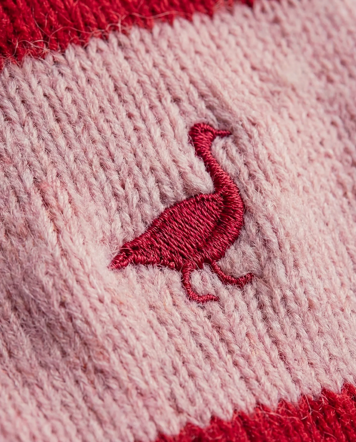 Close-up of pink and red knitted fabric with a red embroidered flamingo design.