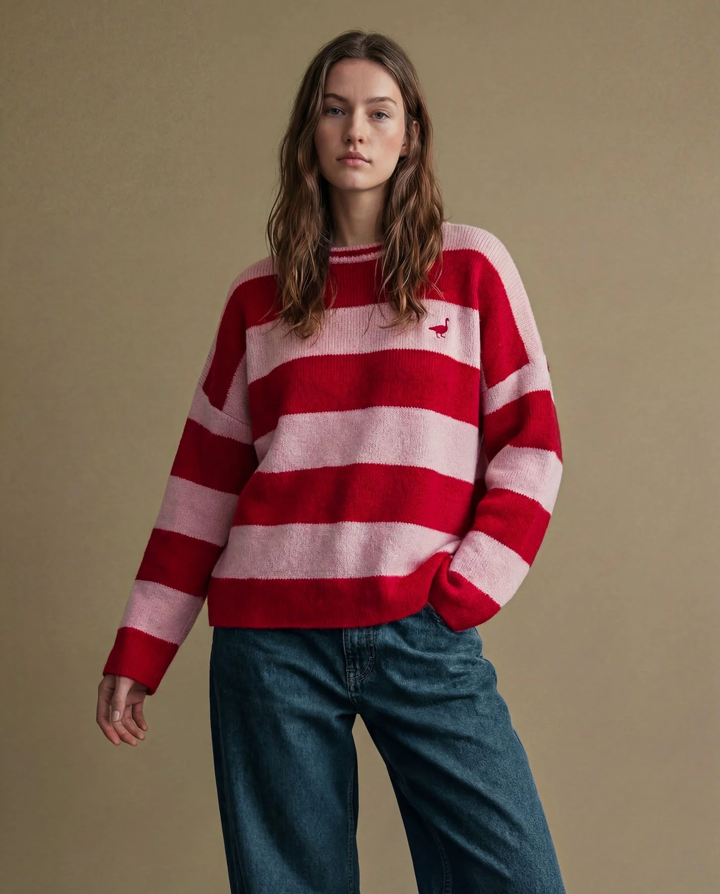 Young woman wearing a red and pink striped sweater and blue jeans, standing against a plain background.