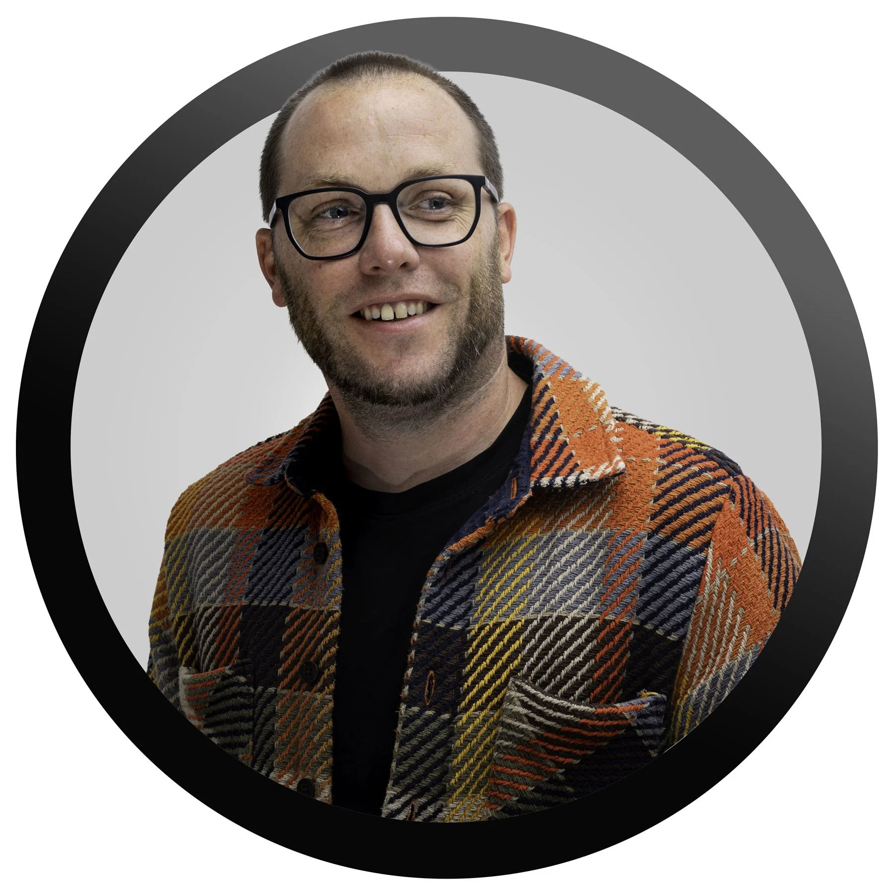 A man with glasses, a beard and short hair smiling, wearing a black shirt and a colorful patterned jacket, against a circular backdrop.