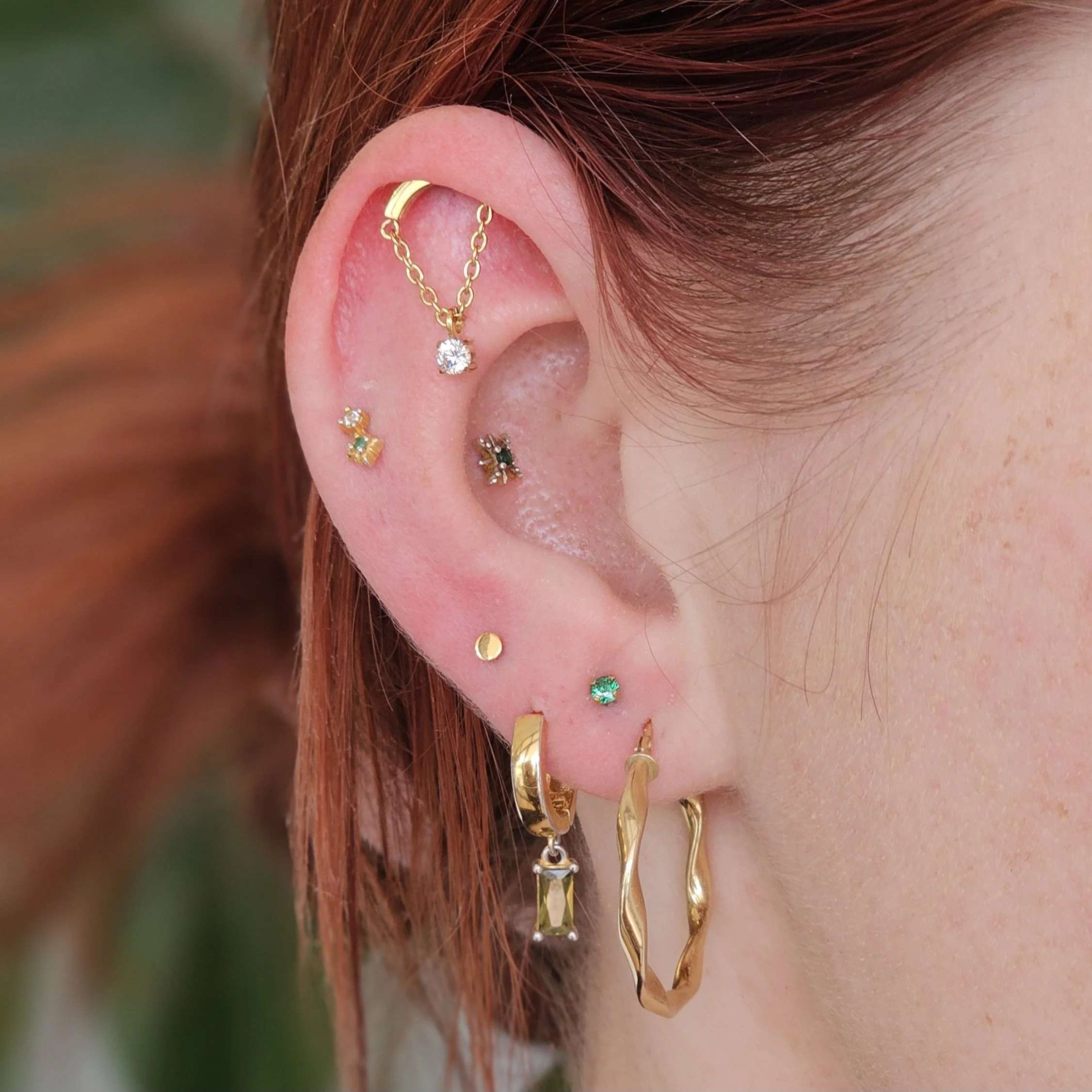 Curated gold pierced ear, green gemstone earrings and gold. Stacked lobe piercing, snakebite helix piercings, and hidden helix piercing. 