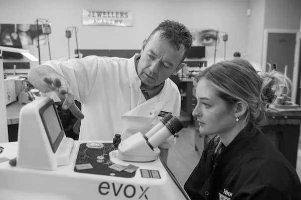 A man in a lab coat shows a woman how to use a microscope in a laboratory.