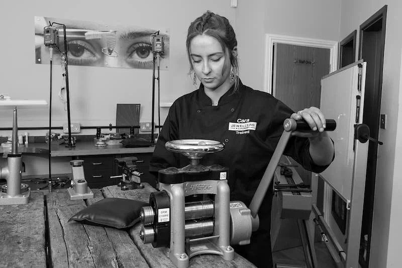 A woman working at a jewelry scale in a workshop, with tools and equipment around her.