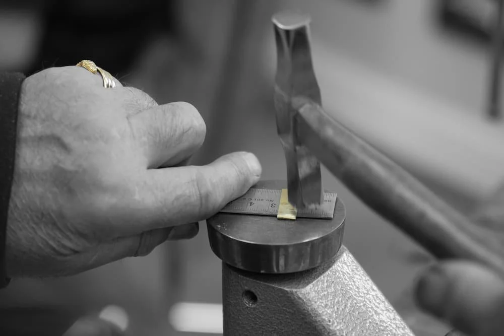 Close-up of a person's hand measuring a metal object with a steel ruler on a workbench, in black and white.
