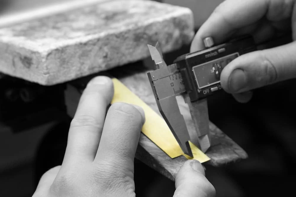 Hands using a digital caliper to measure a yellow object on a workbench.