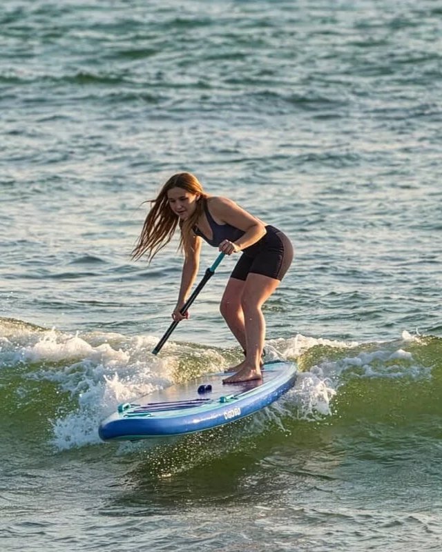 Une femme fait du paddle sur l'eau avec une planche bleue et une pagaie.