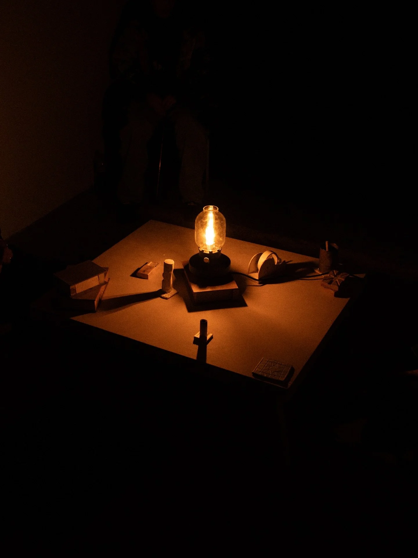 Table with a lantern emitting warm light, surrounded by small objects in a dark room.