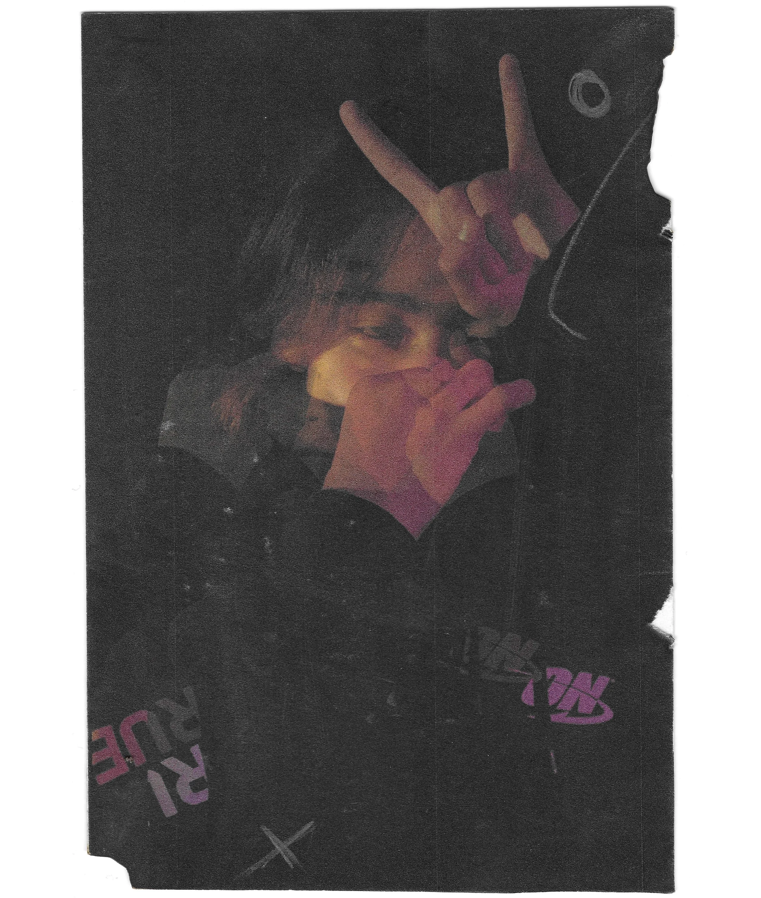 A person making a peace sign and holding a microphone, with a dark background and some text visible on their clothing.