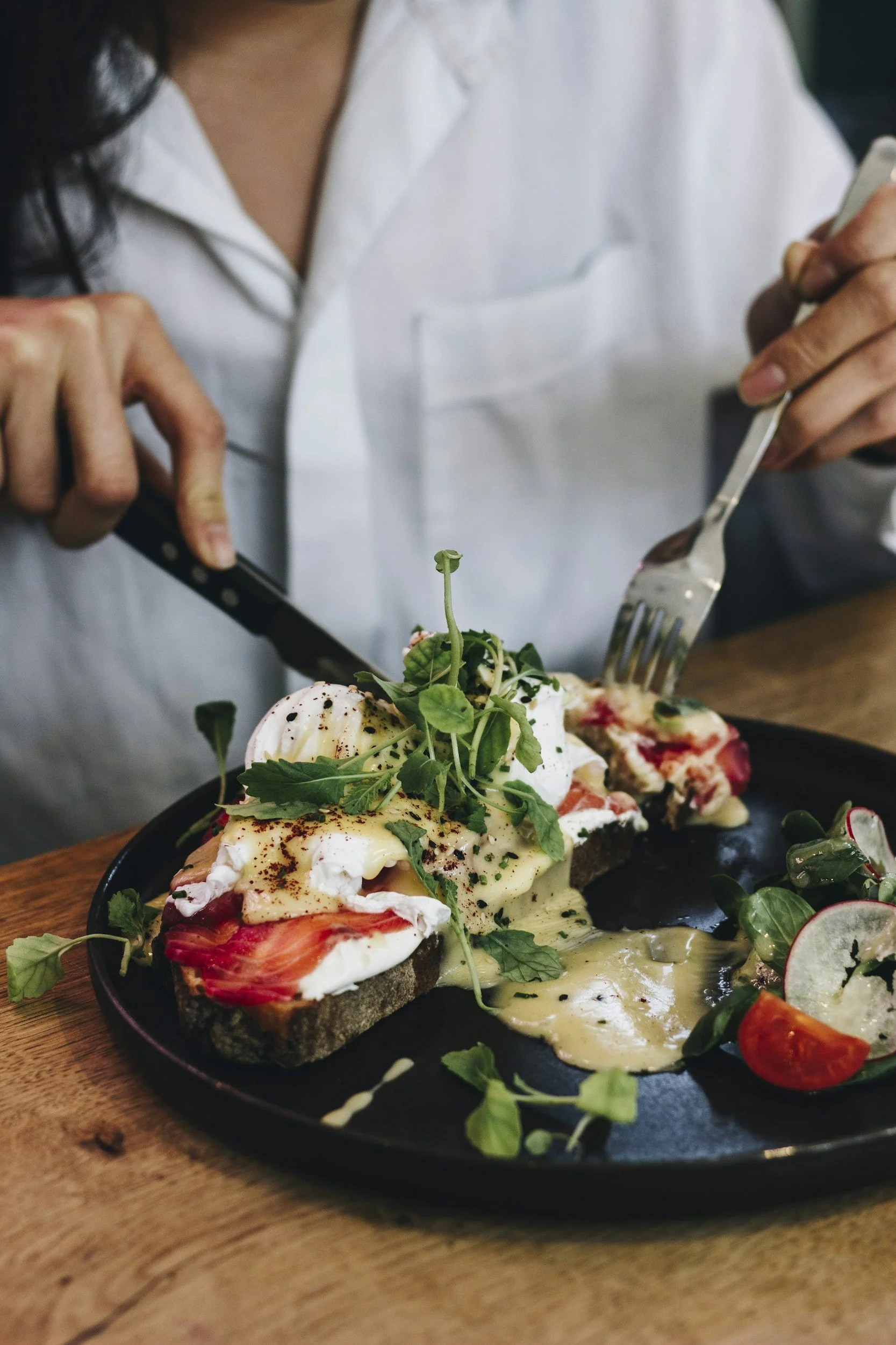 En person spiser en rett med egg, tomater, urter og brød.