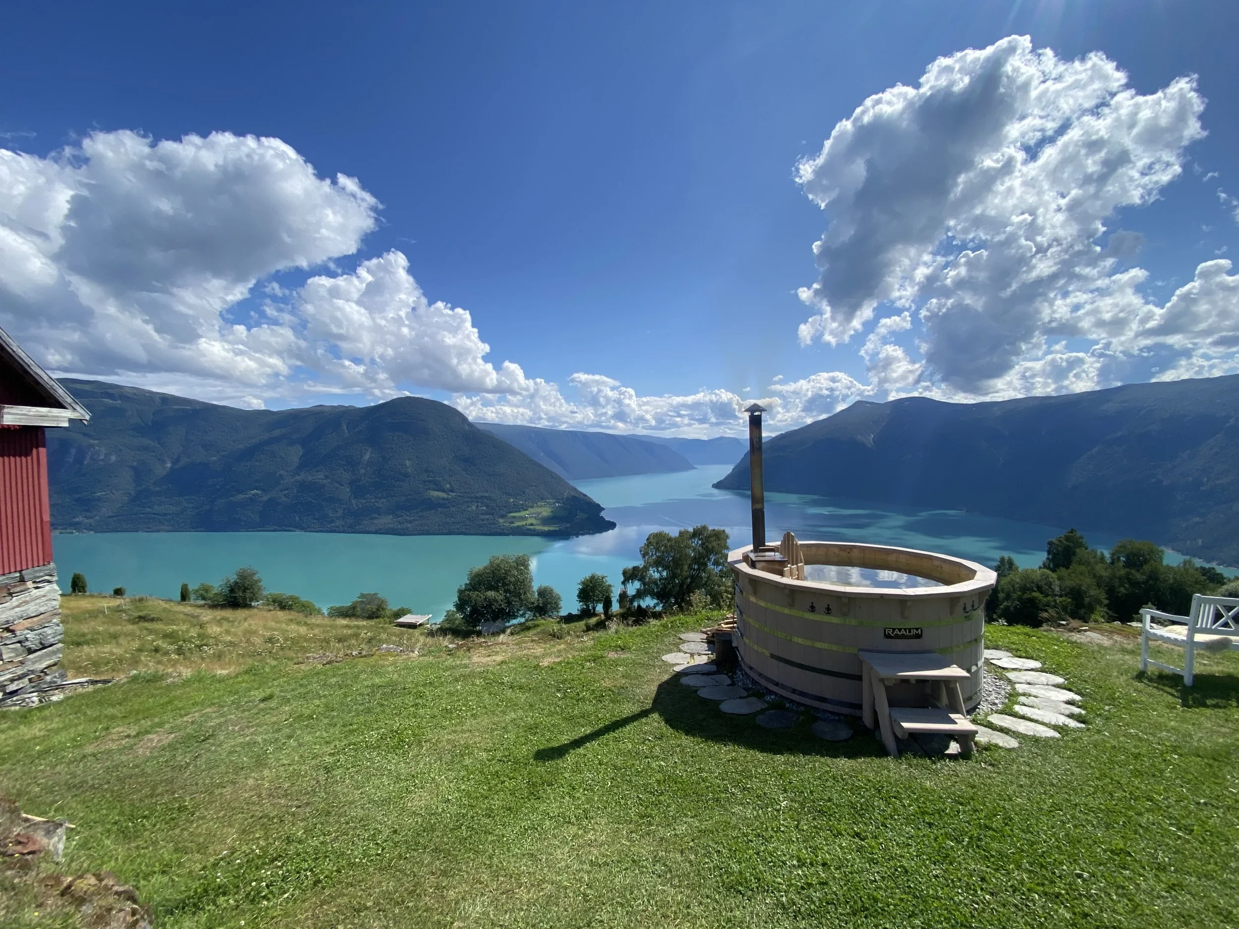 Utsikt over en innsjø omgitt av fjell, med en badestamp i forgrunnen og en liten trebygning på venstre side