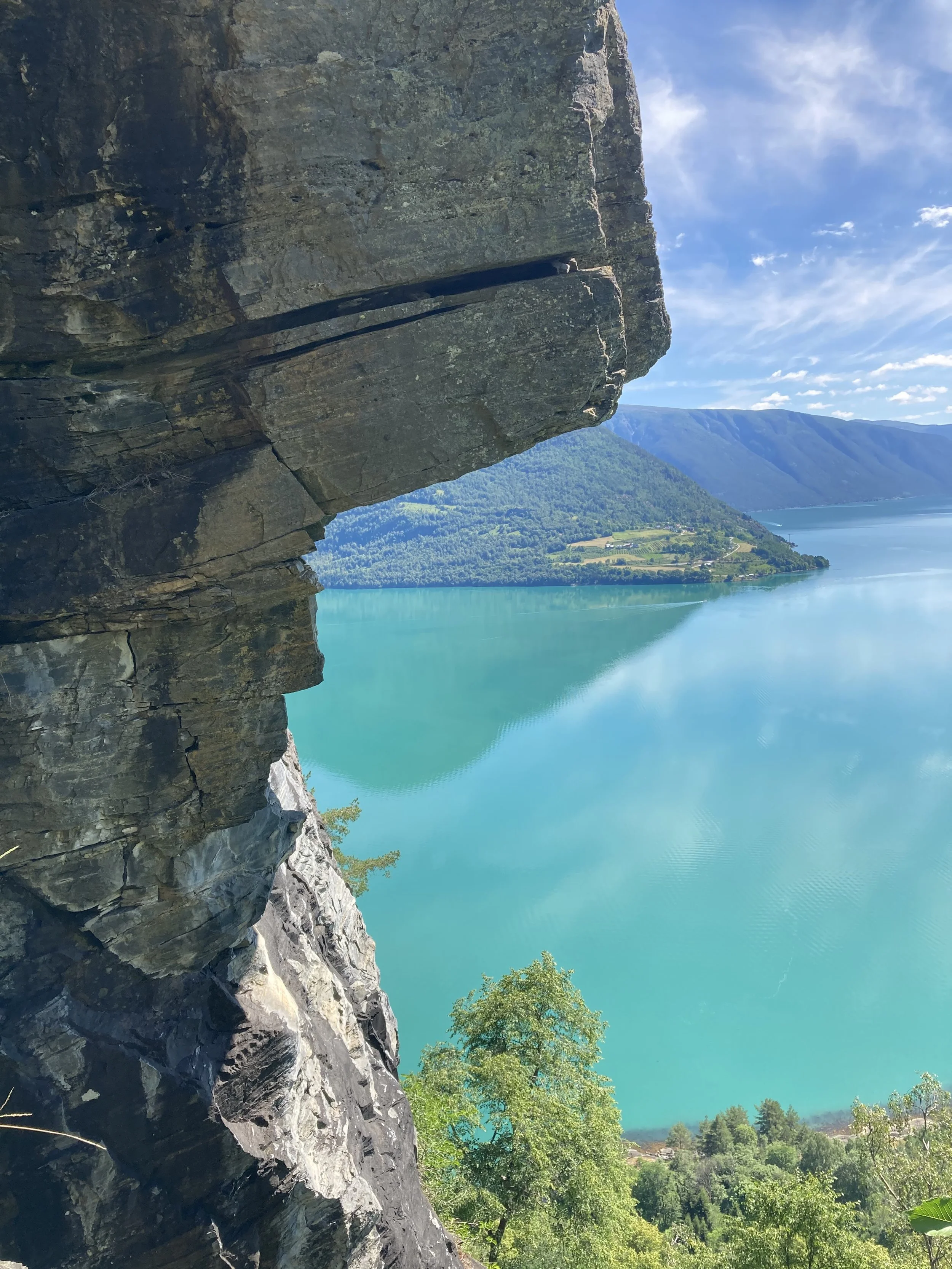 Bergens utsikt over en rolig, turkis innsjø med grønne fjell i bakgrunnen, sett fra en klippe.