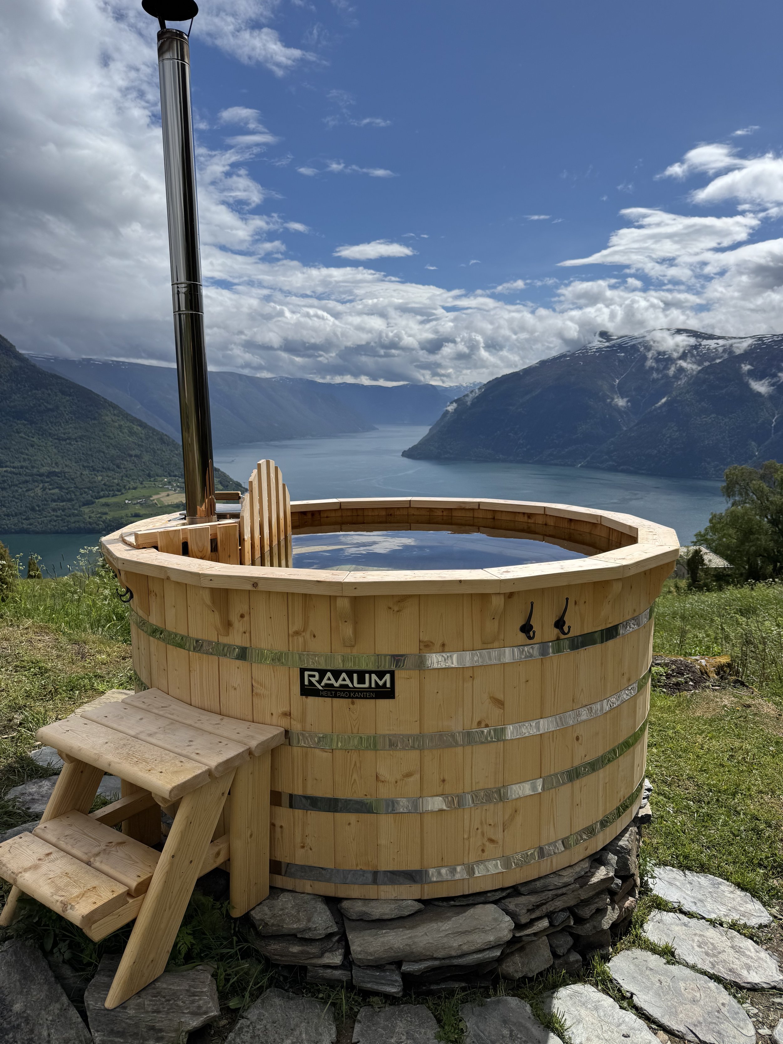 En badestamp laget av tre med utsikt over en fjord og fjell i Norge, med en liten stol foran.