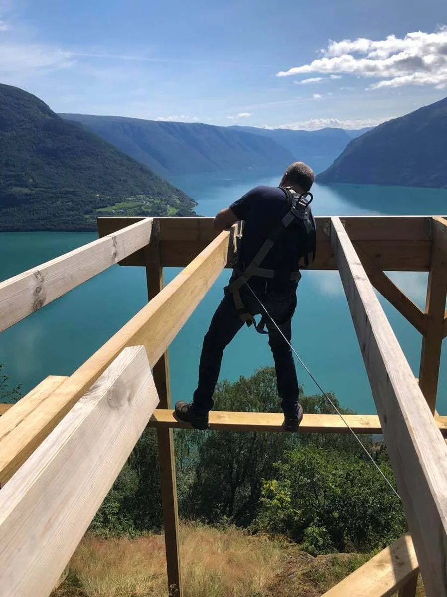 En person som står på en trapp under bygging, med utsikt over en innsjø omgitt av fjell.