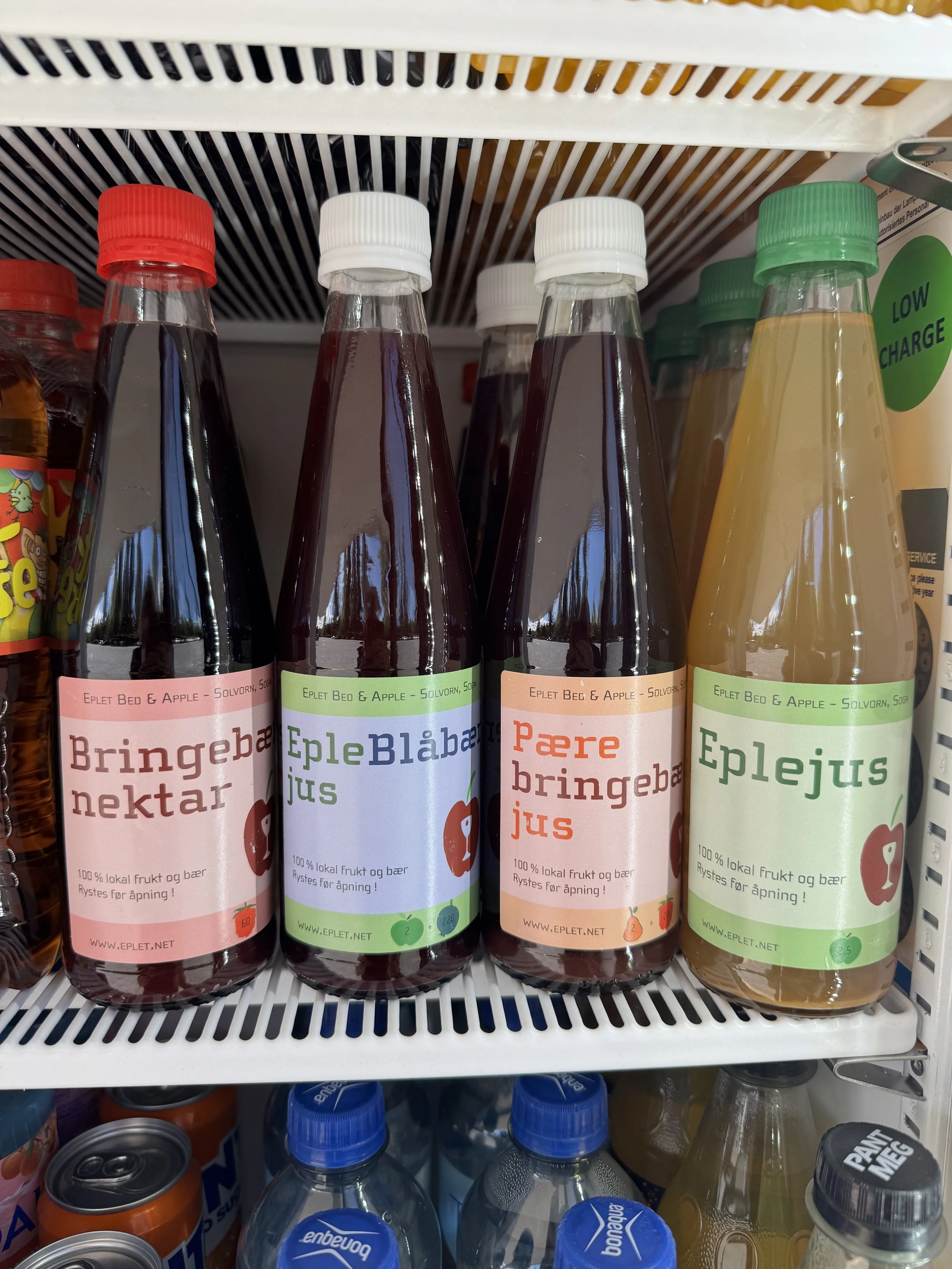 Flasker med ulike sauser eller alkoholer med etiketter på norsk, plassert på butikkhylle.