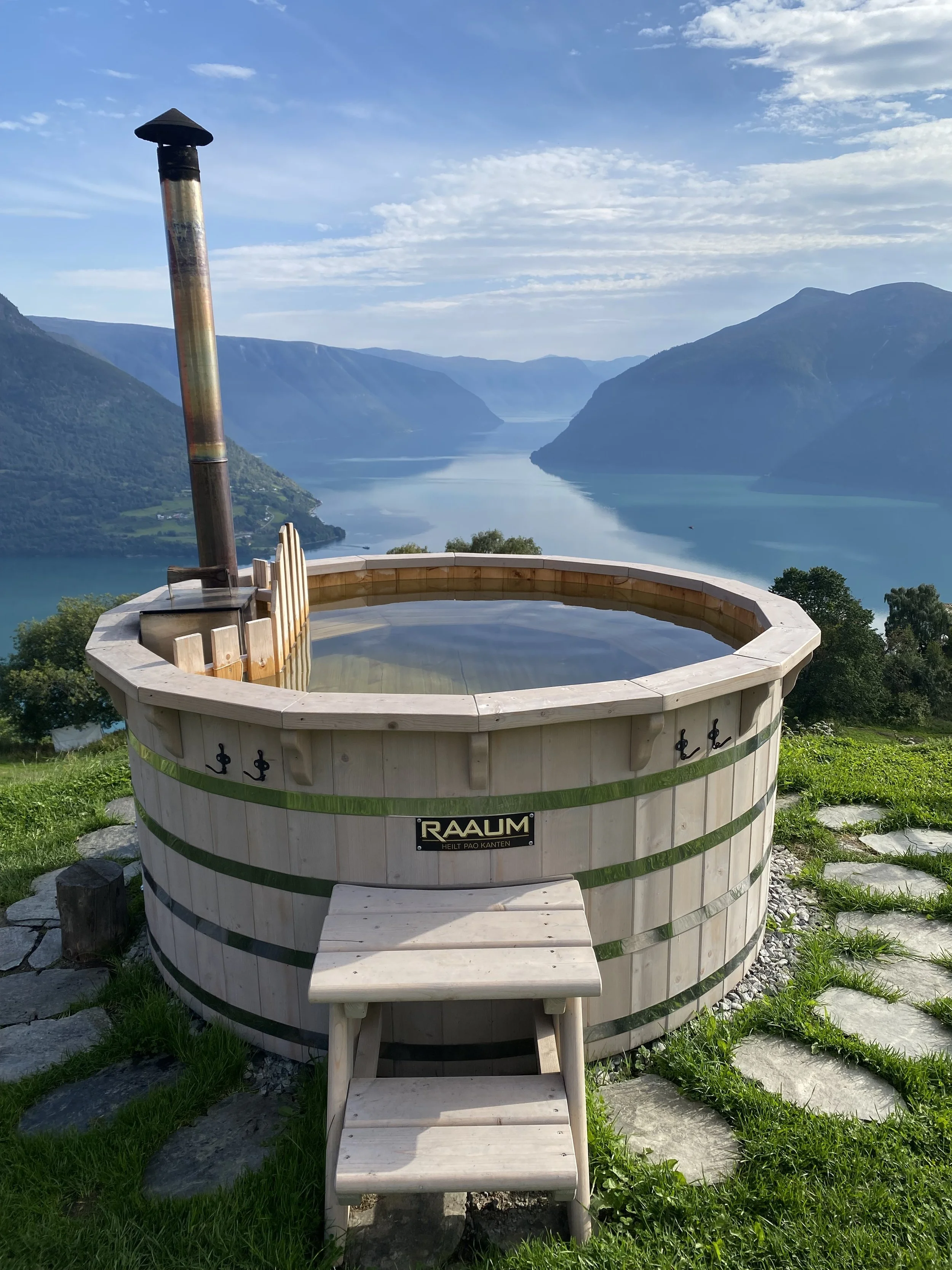 Utedo i tre med utsikt over fjord og fjell, omgitt av grønn vegetasjon.