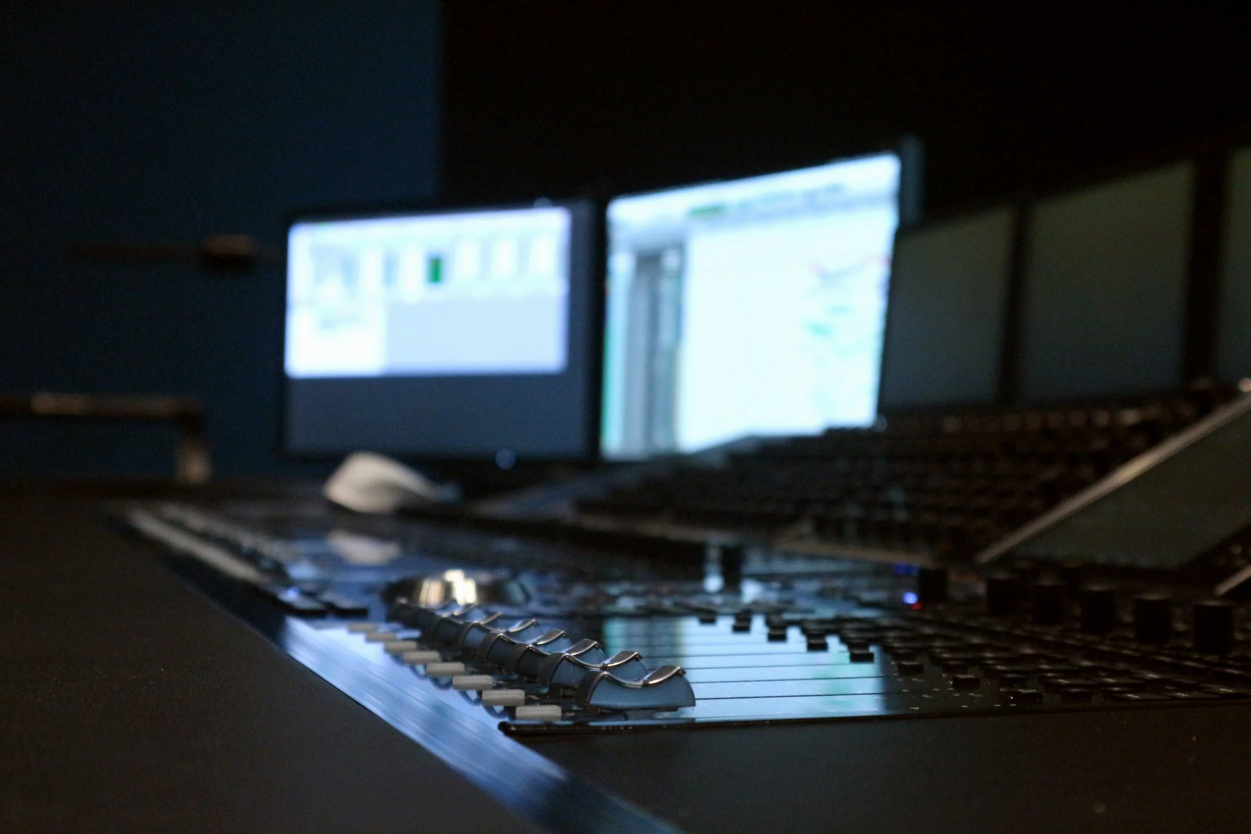 Station de travail de musique avec clavier, moniteurs d'ordinateur, et un ordinateur portable dans une pièce sombre.