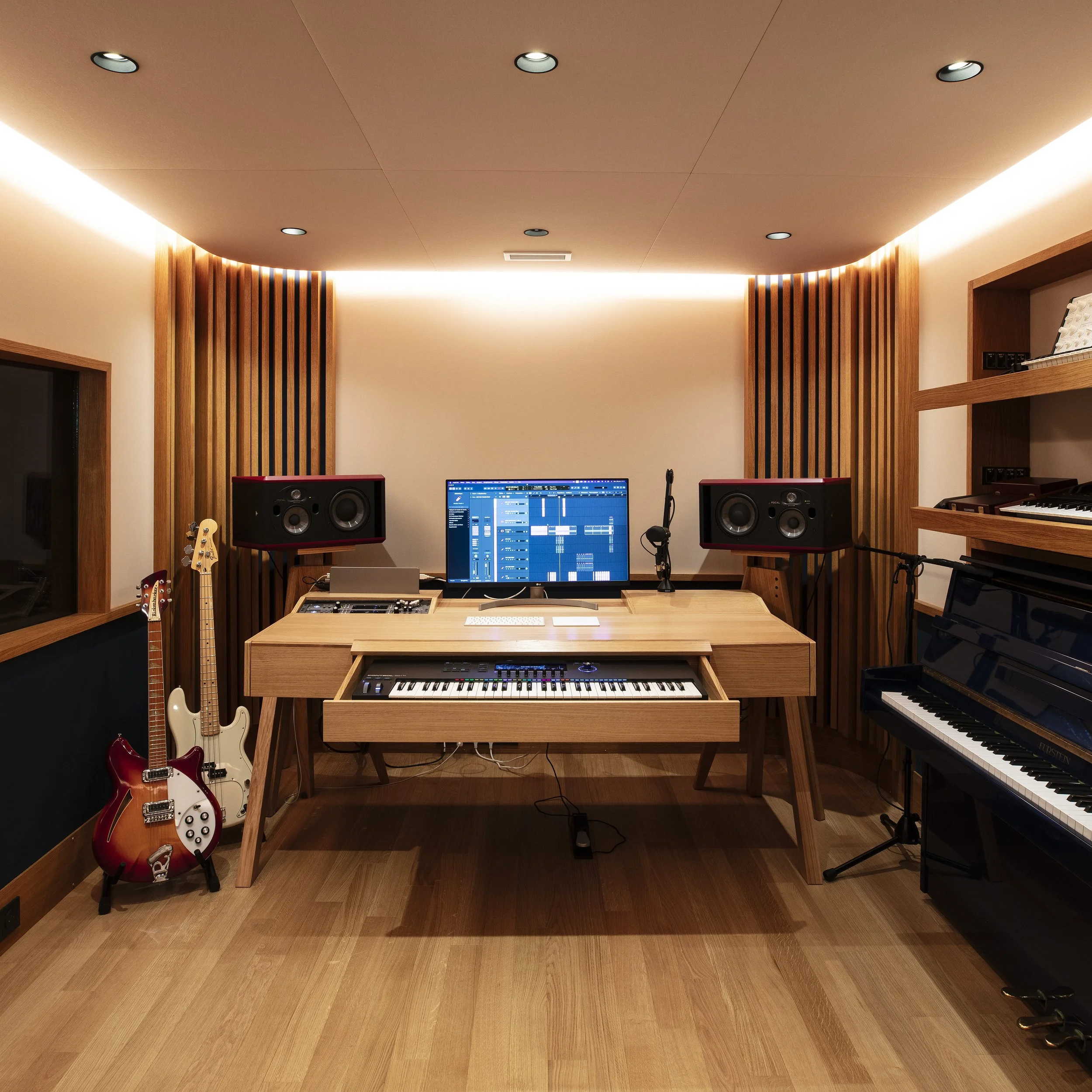 Une salle de studio d'enregistrement avec un piano noir, deux guitares électriques, un ordinateur avec logiciel de musique, deux haut-parleurs, et des étagères avec un clavier et du matériel musical.