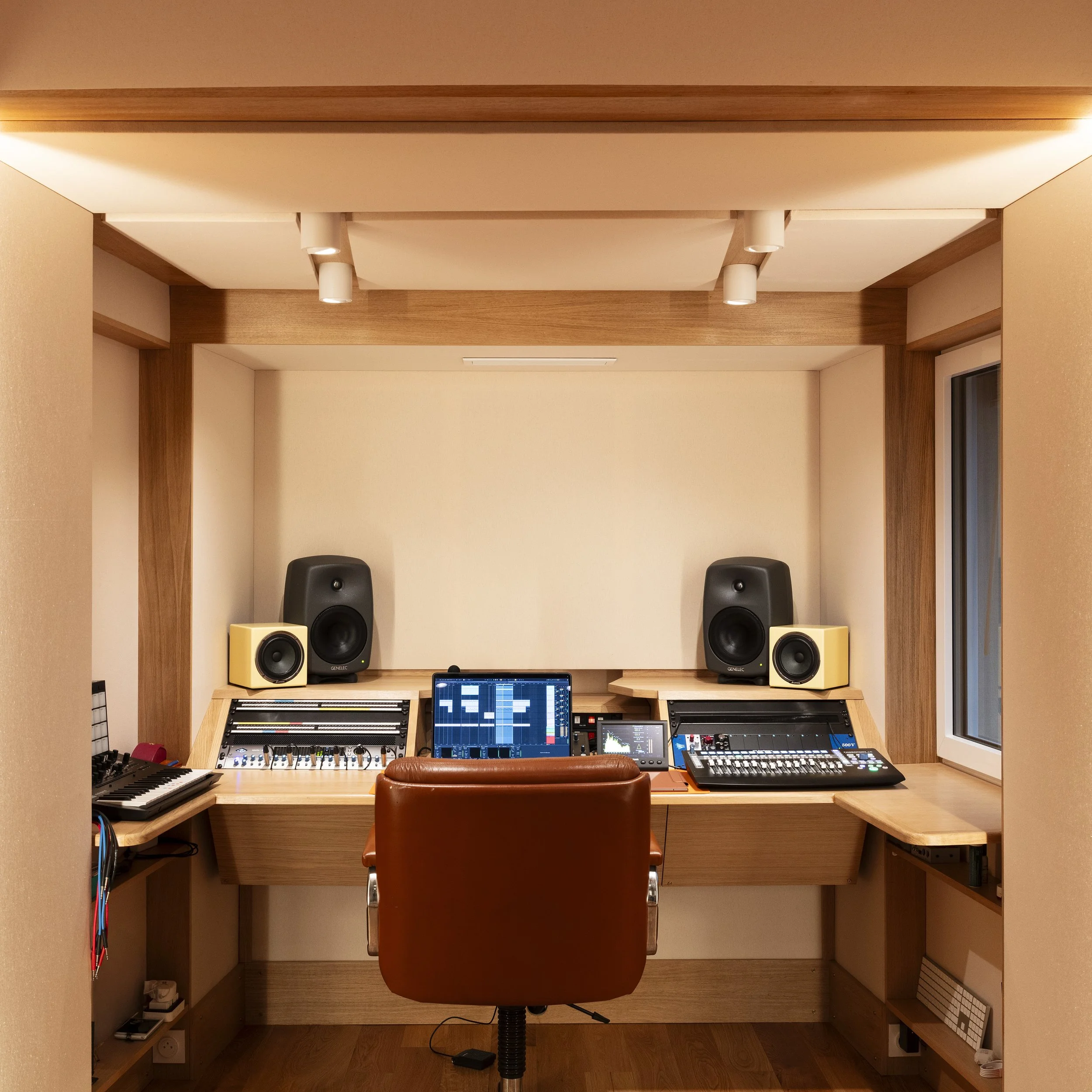 Studio d'enregistrement avec des haut-parleurs, un ordinateur portable avec logiciel de musique, une table de mixage, un clavier contrôleur MIDI, et une chaise en cuir.