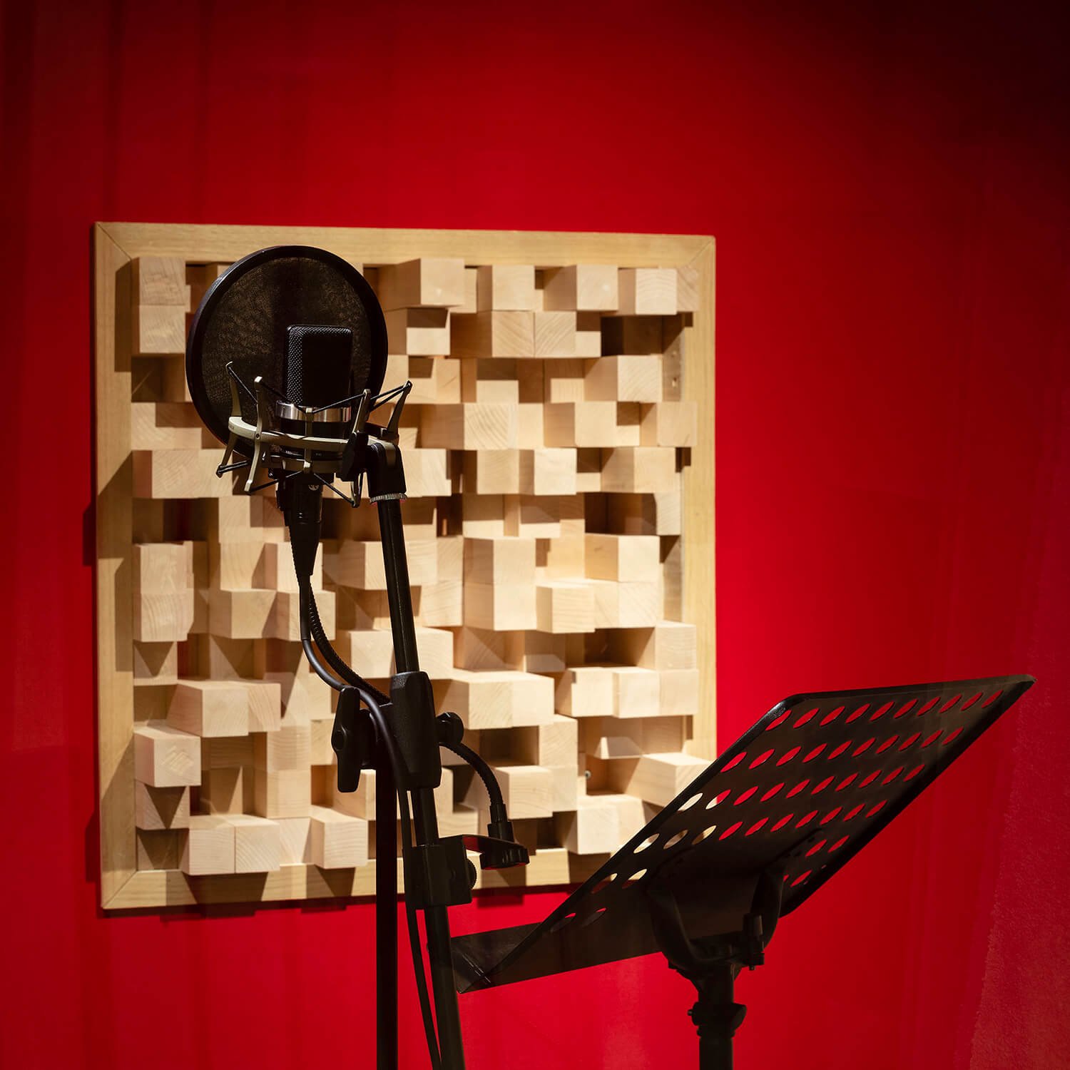 Un microphone devant une cloison acoustique en bois dans une cabine d'enregistrement, avec un pupitre à musique en face, dans une salle de studio avec un mur rouge.