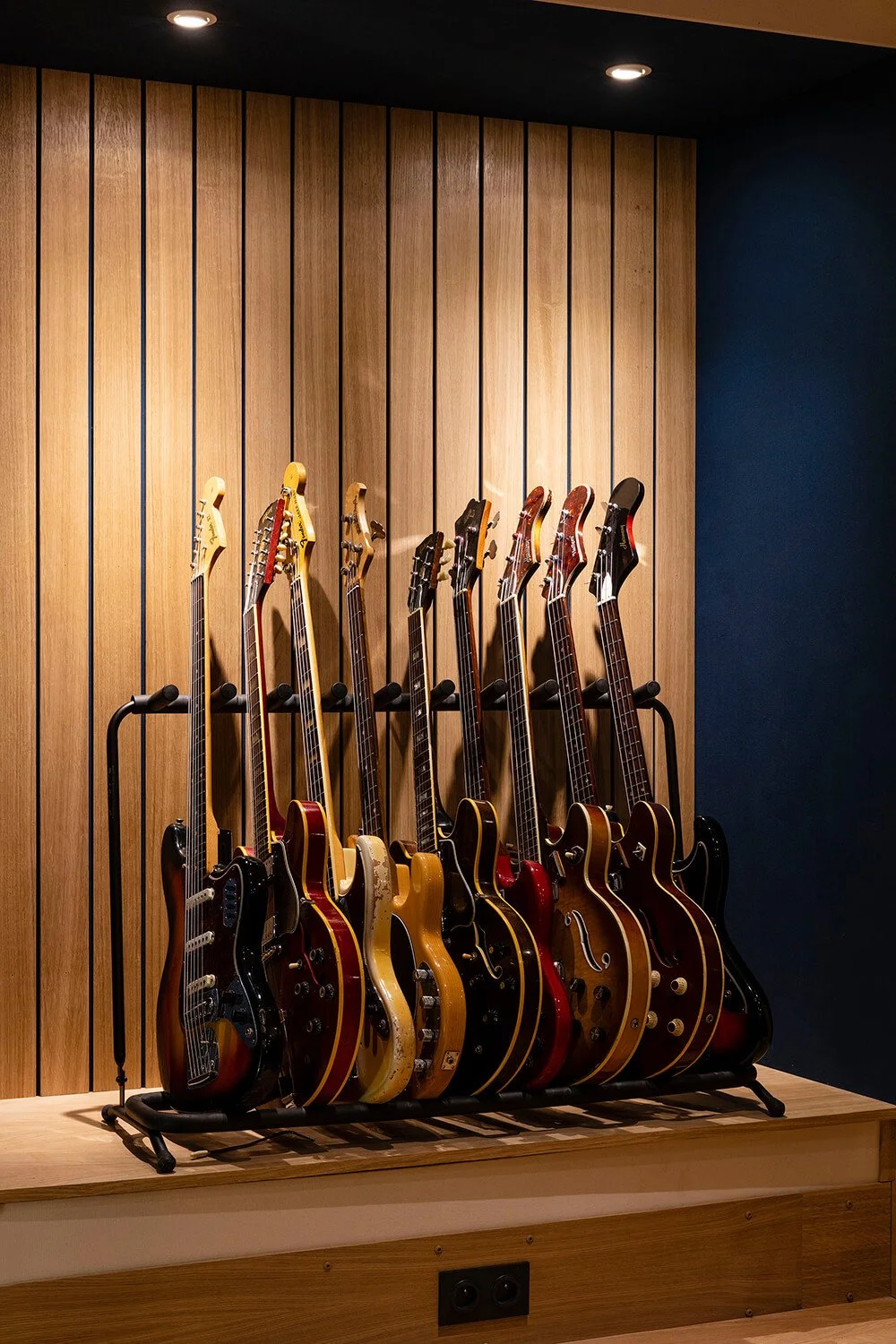 Guitares électriques suspendues sur un support en bois dans une pièce avec un mur en bois et un mur bleu foncé.