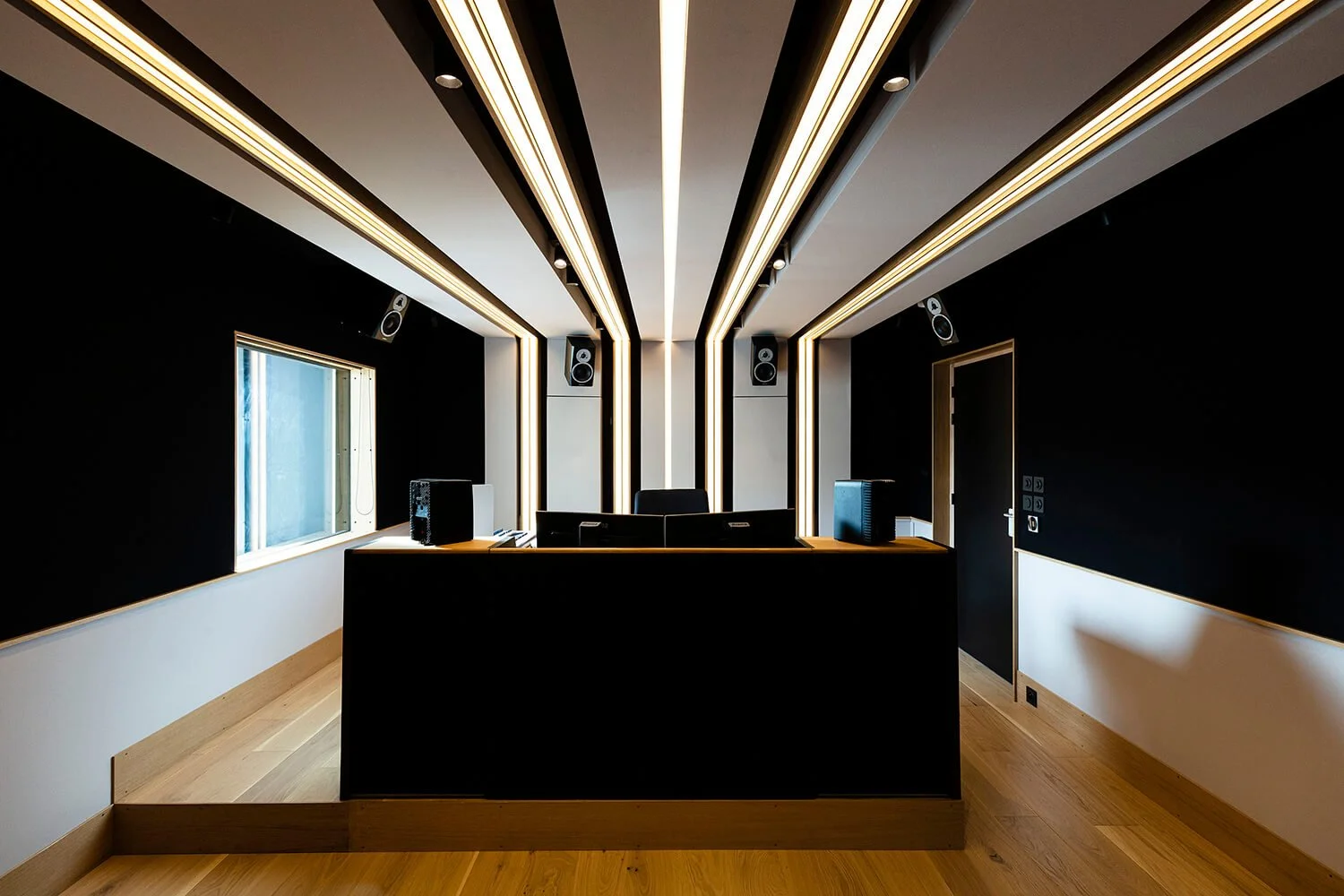 Salle de contrôle avec des haut-parleurs, une fenêtre, et un bureau avec équipements audio dans une pièce moderne.