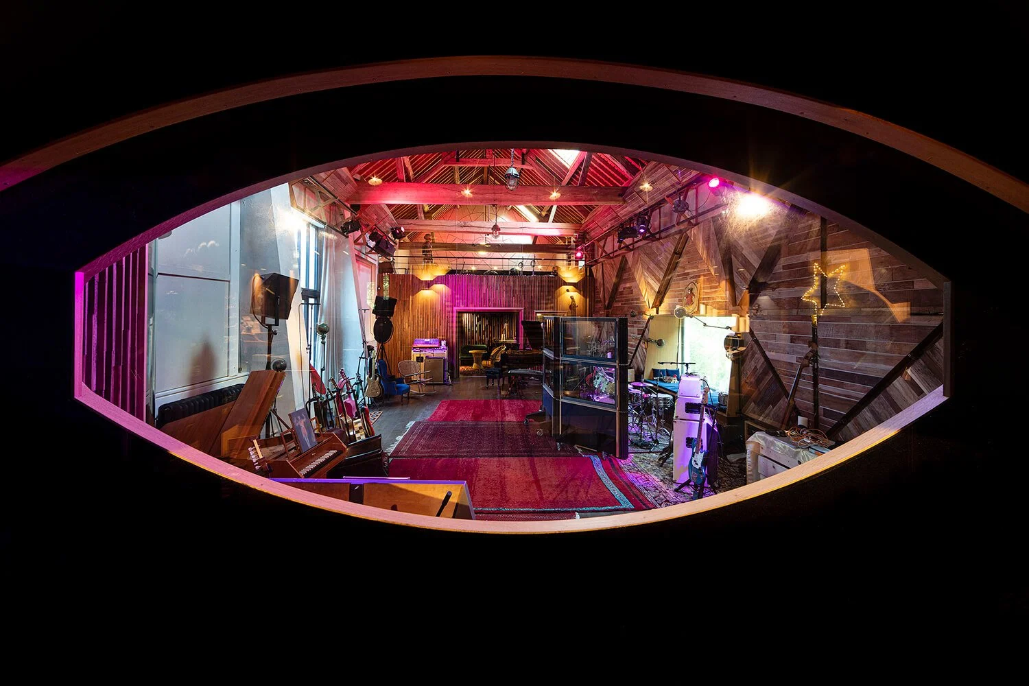 Une salle de studio d'enregistrement avec instruments de musique, microphones, équipements audio, un piano et une ambiance éclairée de lumières colorées.