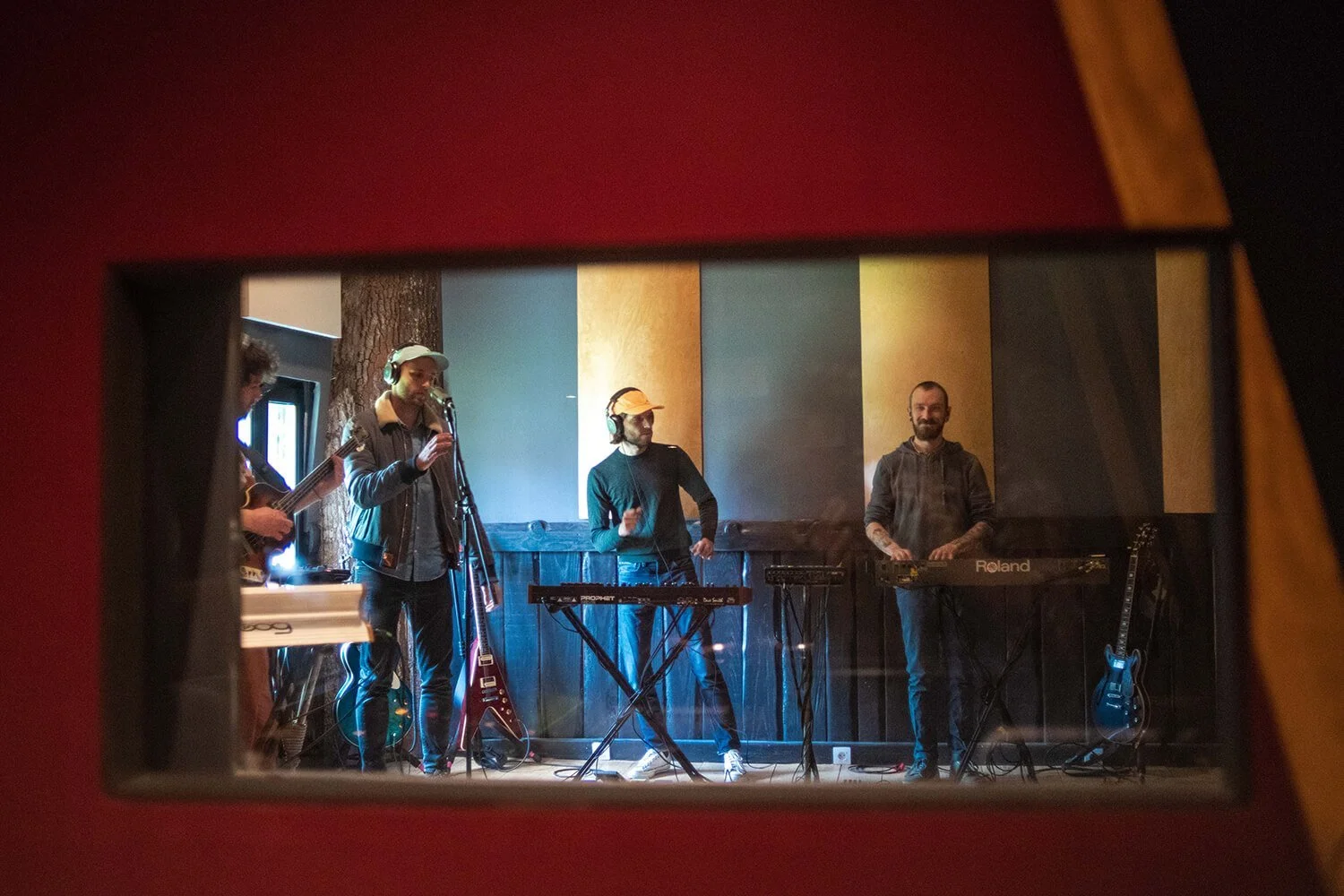 Groupe de musiciens en studio d'enregistrement, jouant de divers instruments comme clavier, guitare et percussions, vue par un trou de serrure.