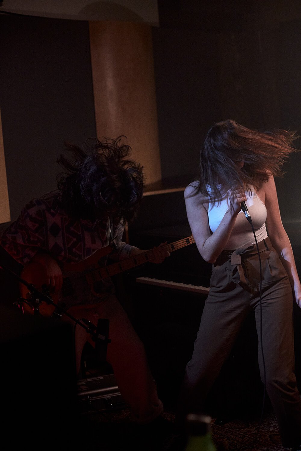 Deux femmes jouent de la musique dans une pièce sombre, l'une à la guitare et l'autre au micro.