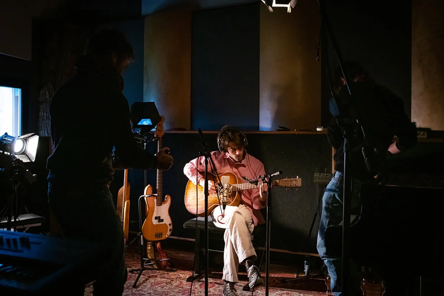 Musicien jouant de la guitare dans un studio d'enregistrement avec des équipes techniques autour.