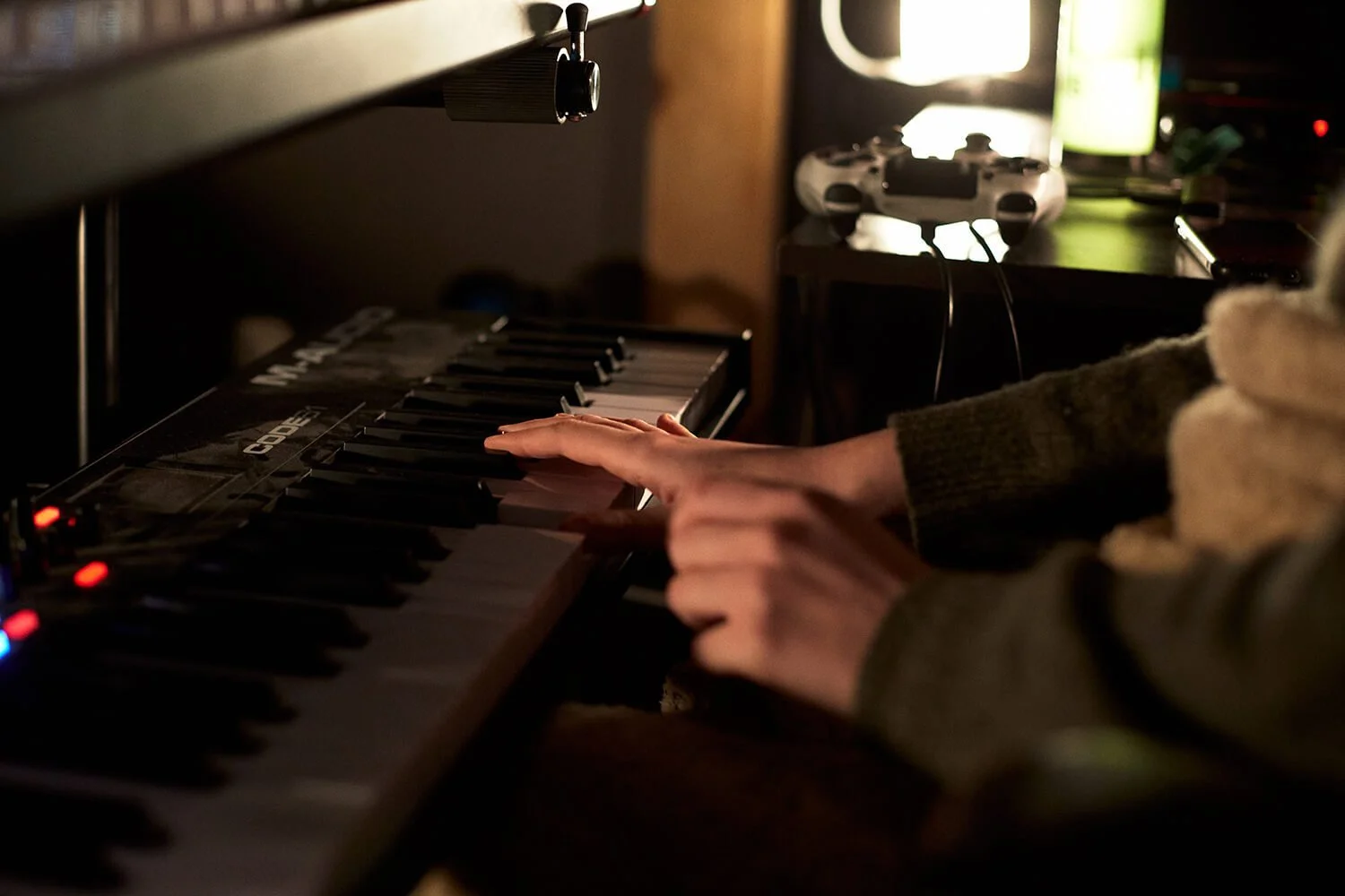 Une personne joue du clavier numérique dans une pièce sombre, avec une console de jeu et un téléviseur à l'arrière-plan.