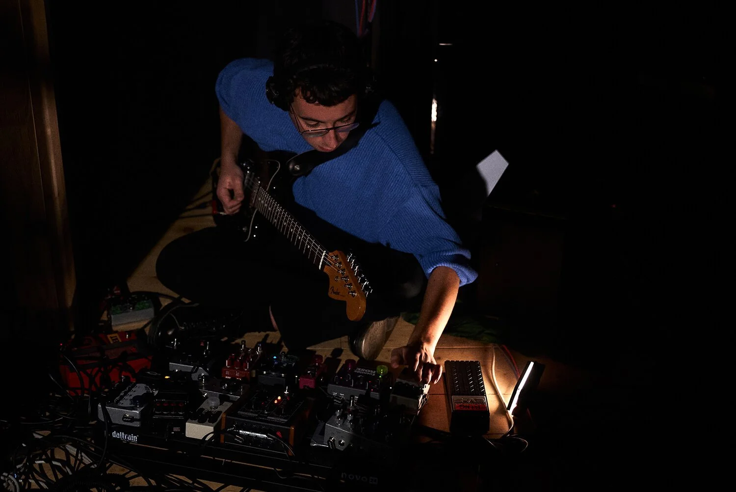 Musicien jouant de la guitare électrique dans un environnement sombre avec des appareils de musique électronique sur une table.
