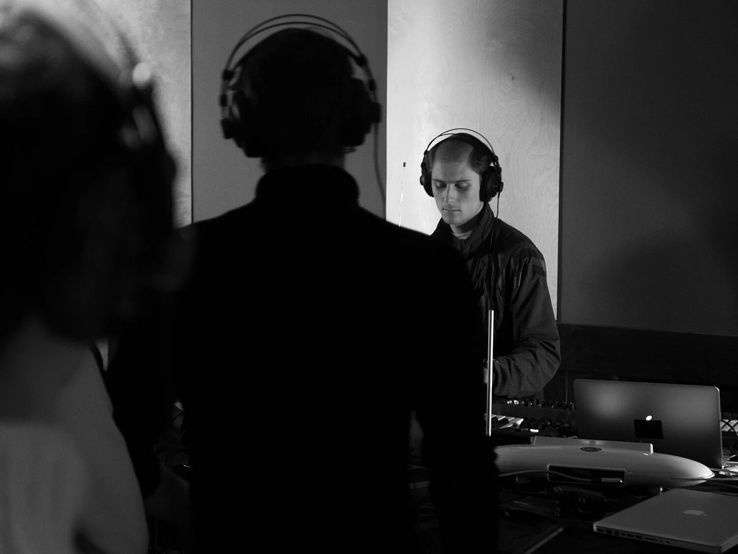 Trois personnes portant des casques audio dans une salle sombre, avec un ordinateur portable et du matériel de musique sur une table.