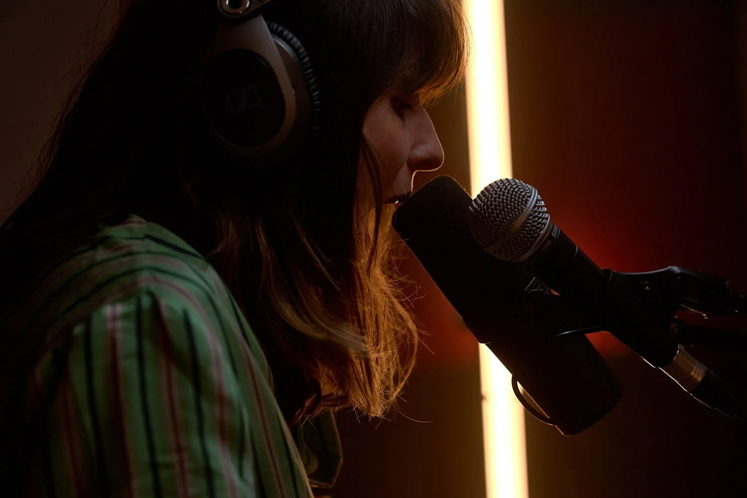 Femme chantant ou parlant dans un microphone avec un casque, en intérieur, éclairage tamisé