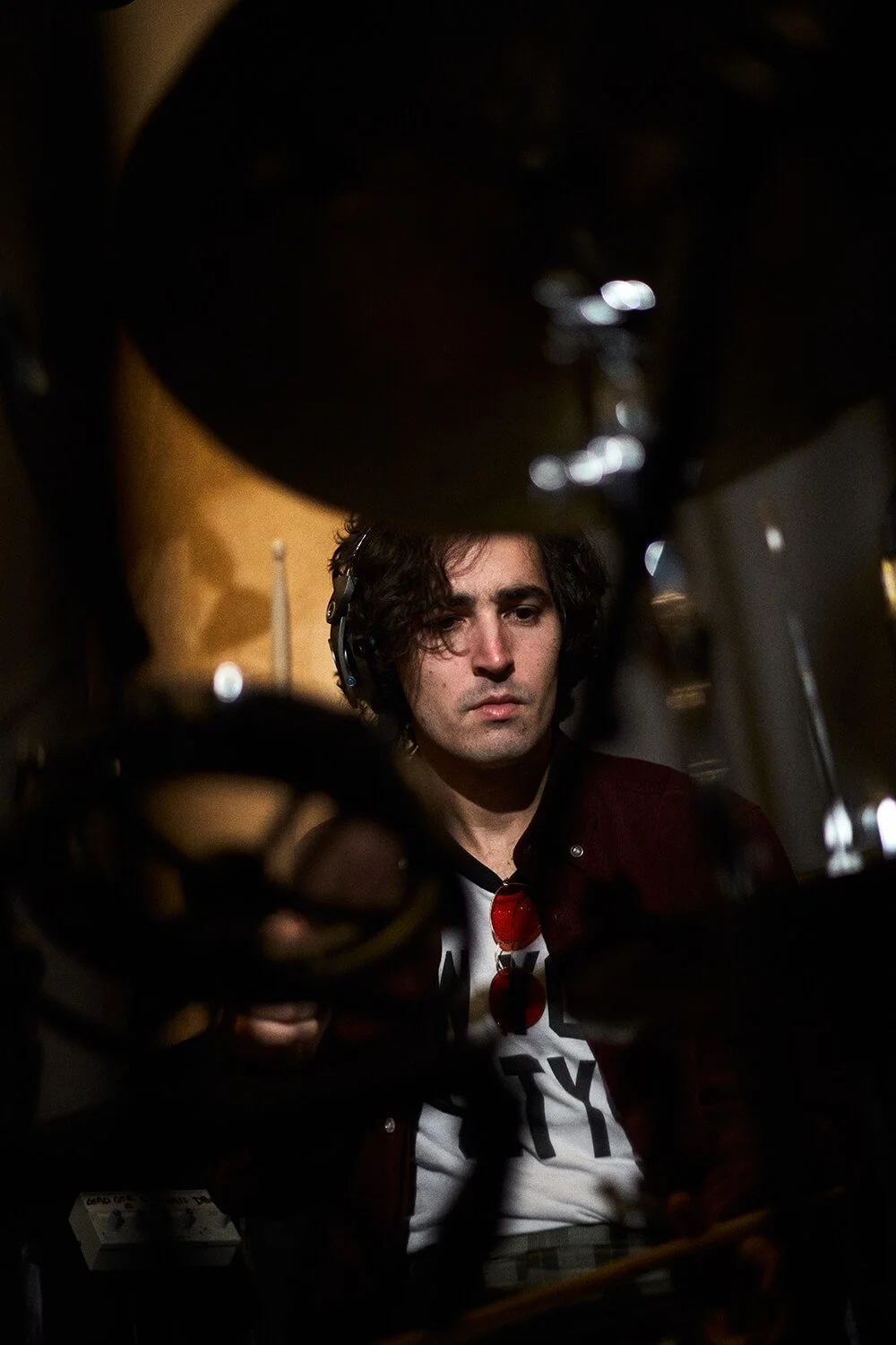 Un homme avec des cheveux bouclés foncés portant un casque, vu à travers un obstacle noir, regarde attentivement quelque chose.