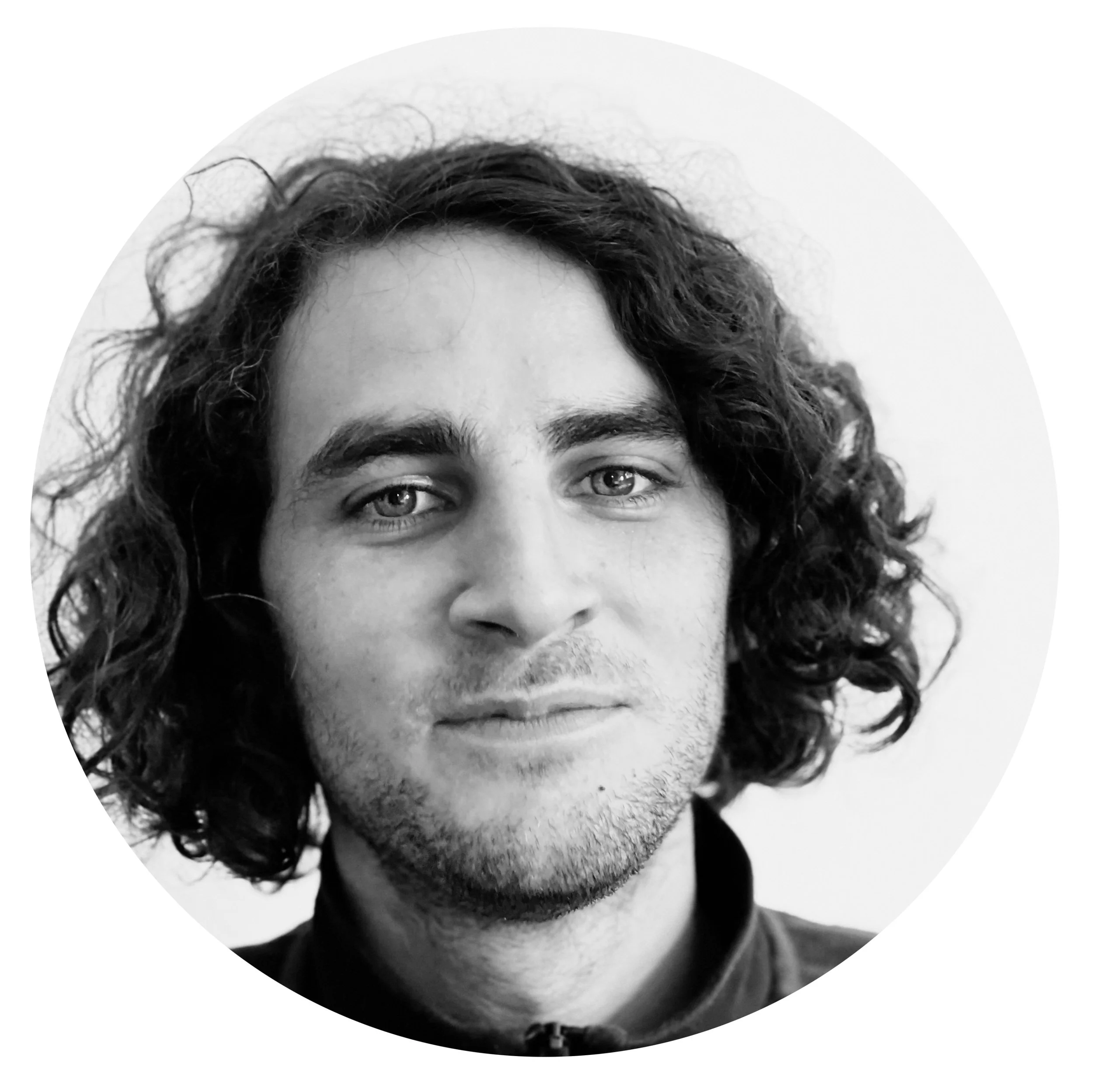 Portrait en noir et blanc d'un jeune homme avec des cheveux longs et bouclés, regardant vers l'objectif.