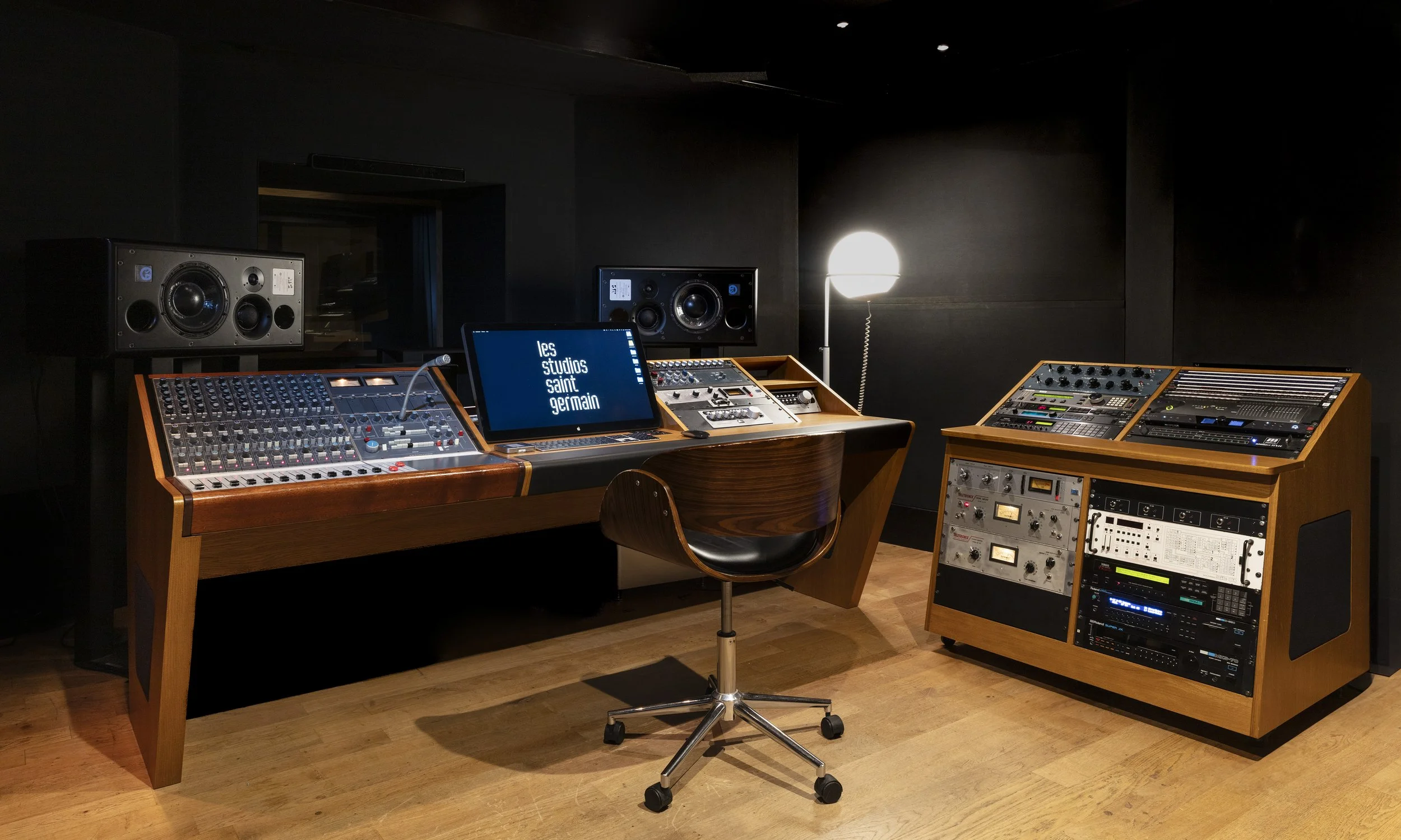 Salle de studio d'enregistrement avec équipements audio, consoles, haut-parleurs, mobilier en bois, lampe et ordinateur