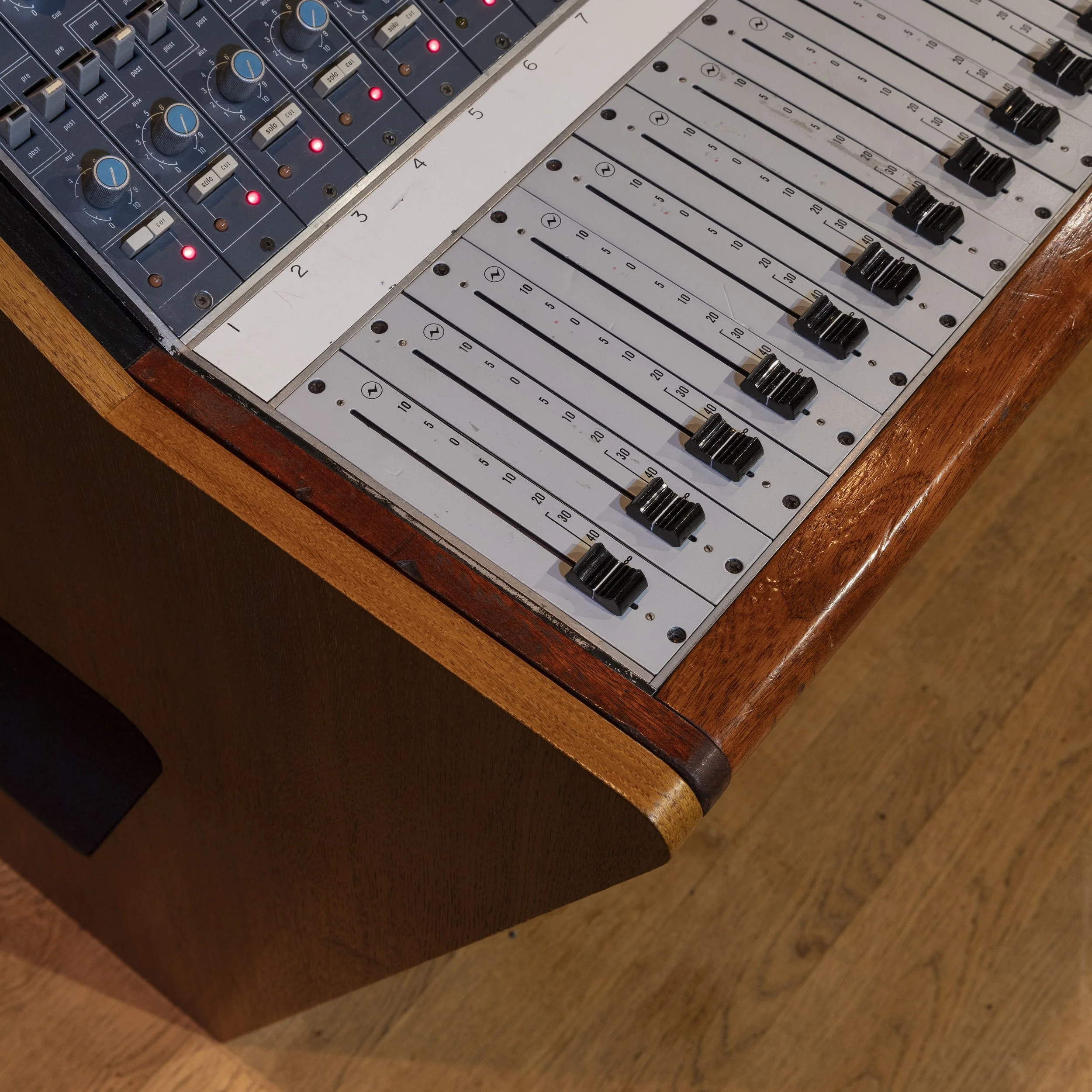 Table de mixage audio avec plusieurs faders, boutons et lumières, en bois.
