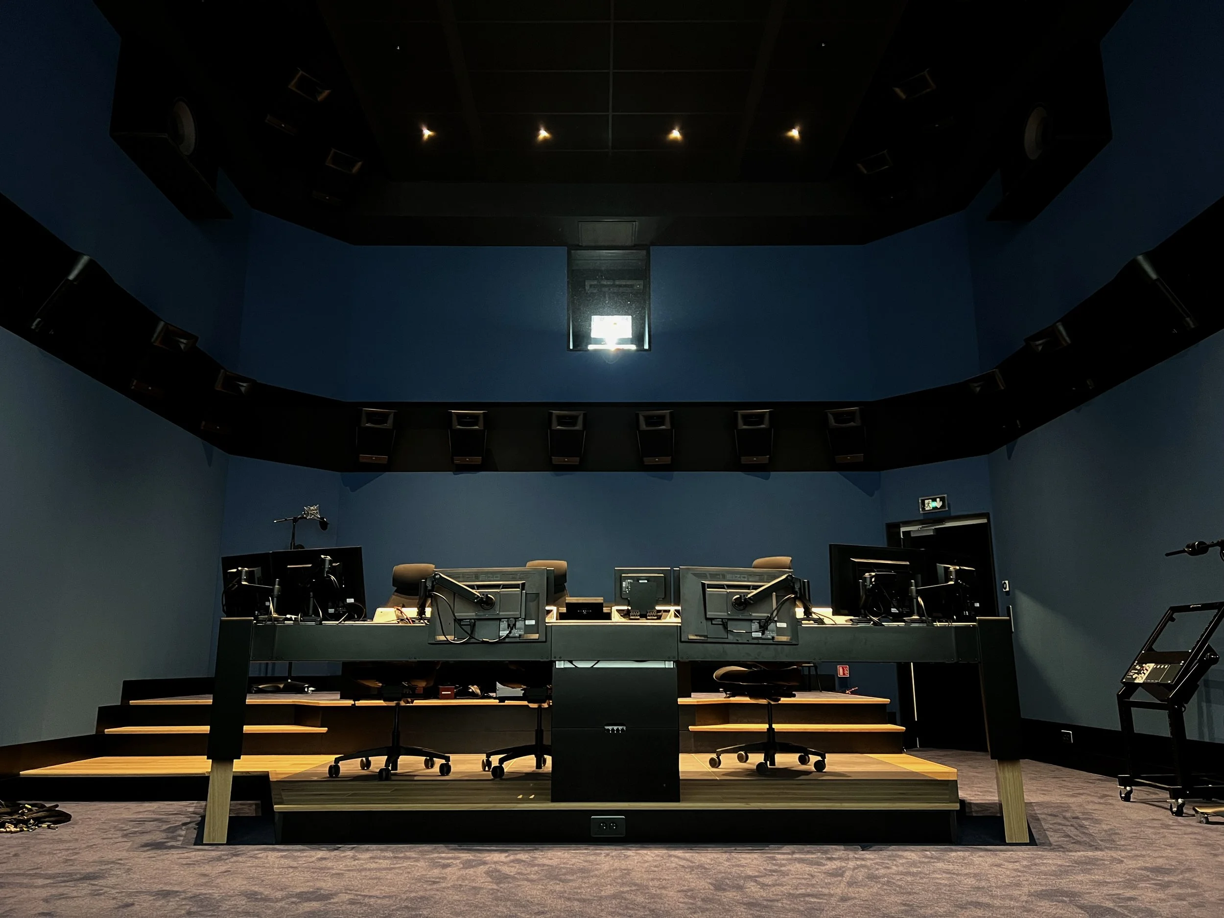 Une salle de conférence ou de studio avec un plateau de discussion équipé de plusieurs ordinateurs, microphones, et chaises, dans une pièce aux murs bleu foncé.