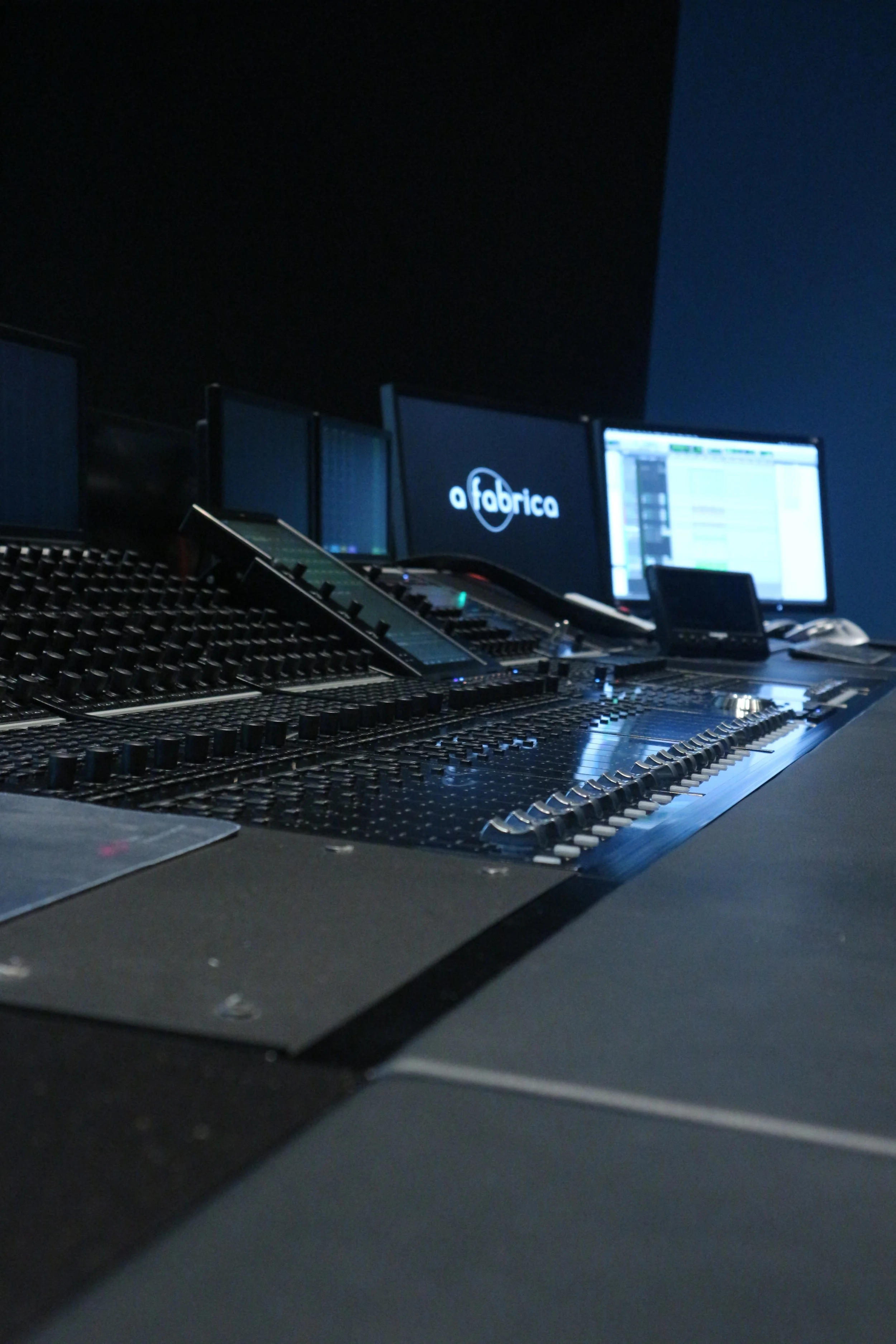 Studio d'enregistrement avec console de mixage, plusieurs écrans et un logo 'a fabrica' affiché sur un écran.