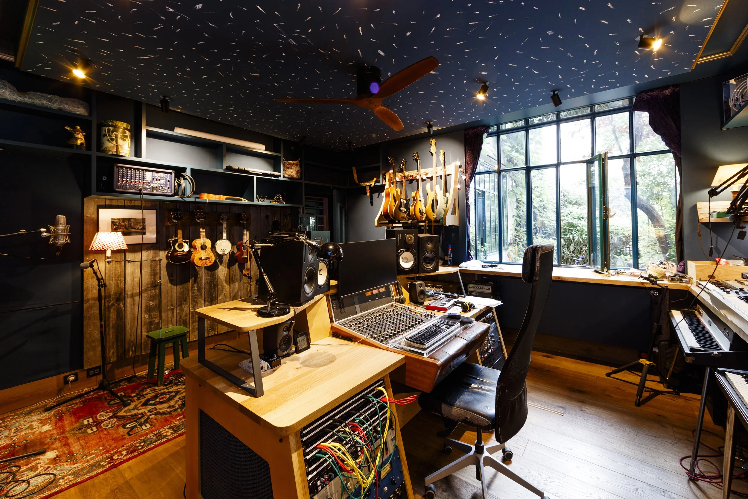 Studio d'enregistrement avec instruments de musique, consoles, enceintes, et une grande fenêtre donnant sur l'extérieur