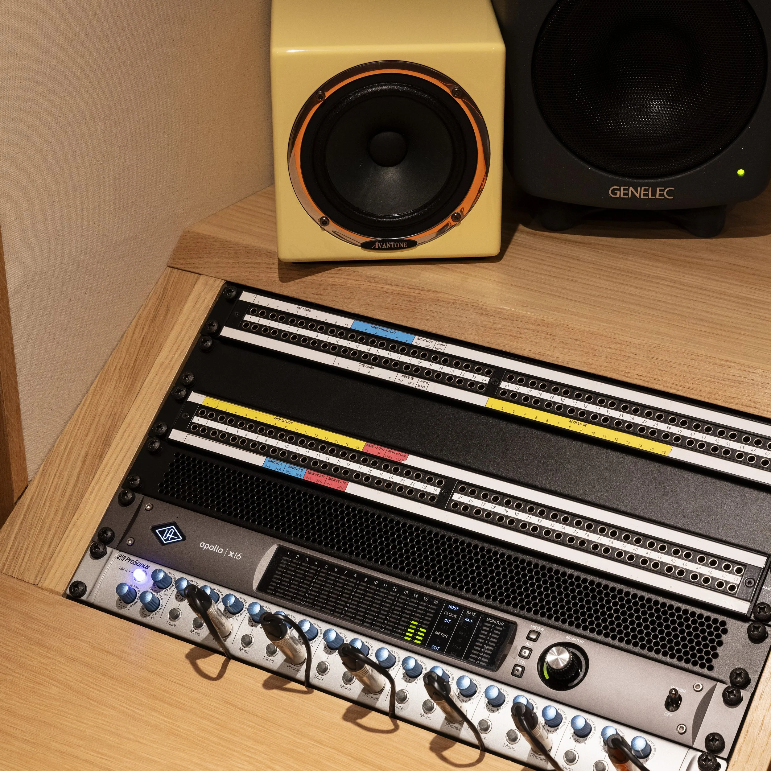 Table de mixage audio avec plusieurs réglages et câbles connectés, deux haut-parleurs en arrière, un jaune et un noir, sur un bureau en bois.