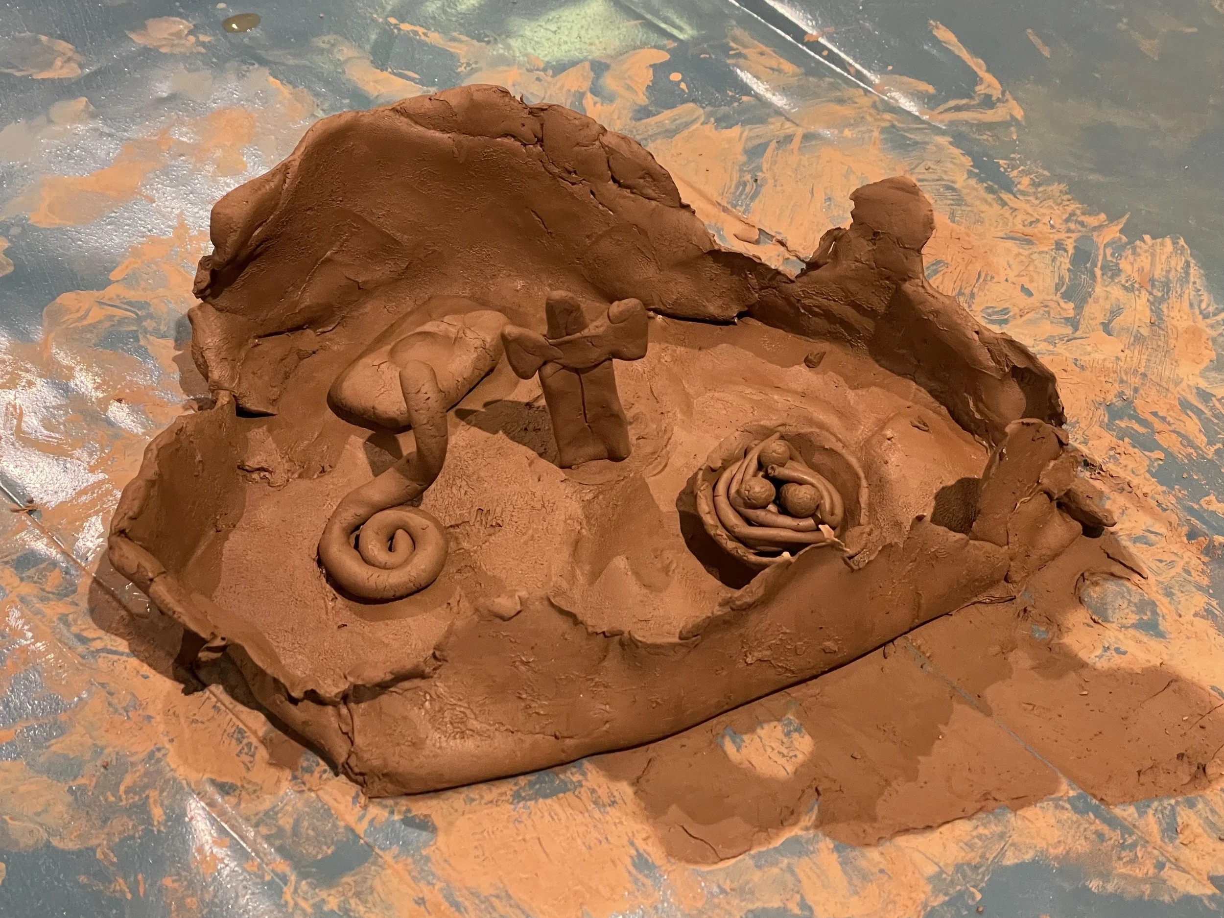Abstract clay sculpture of a eggs in a nest, with a snake nearby, all crafted from brown clay.