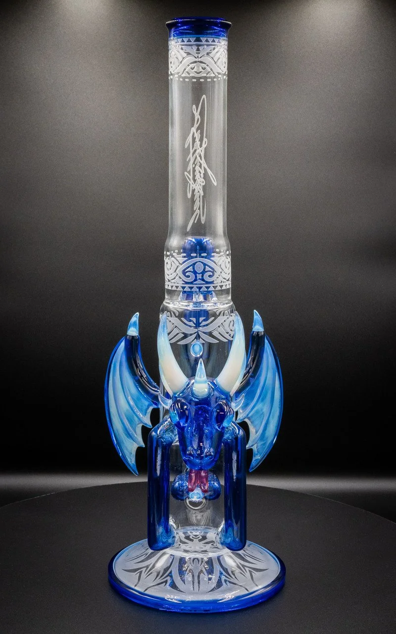 A decorative glass sculpture of a dragon with blue and clear glass, featuring wings, horns, and detailed patterns, set against a dark background.