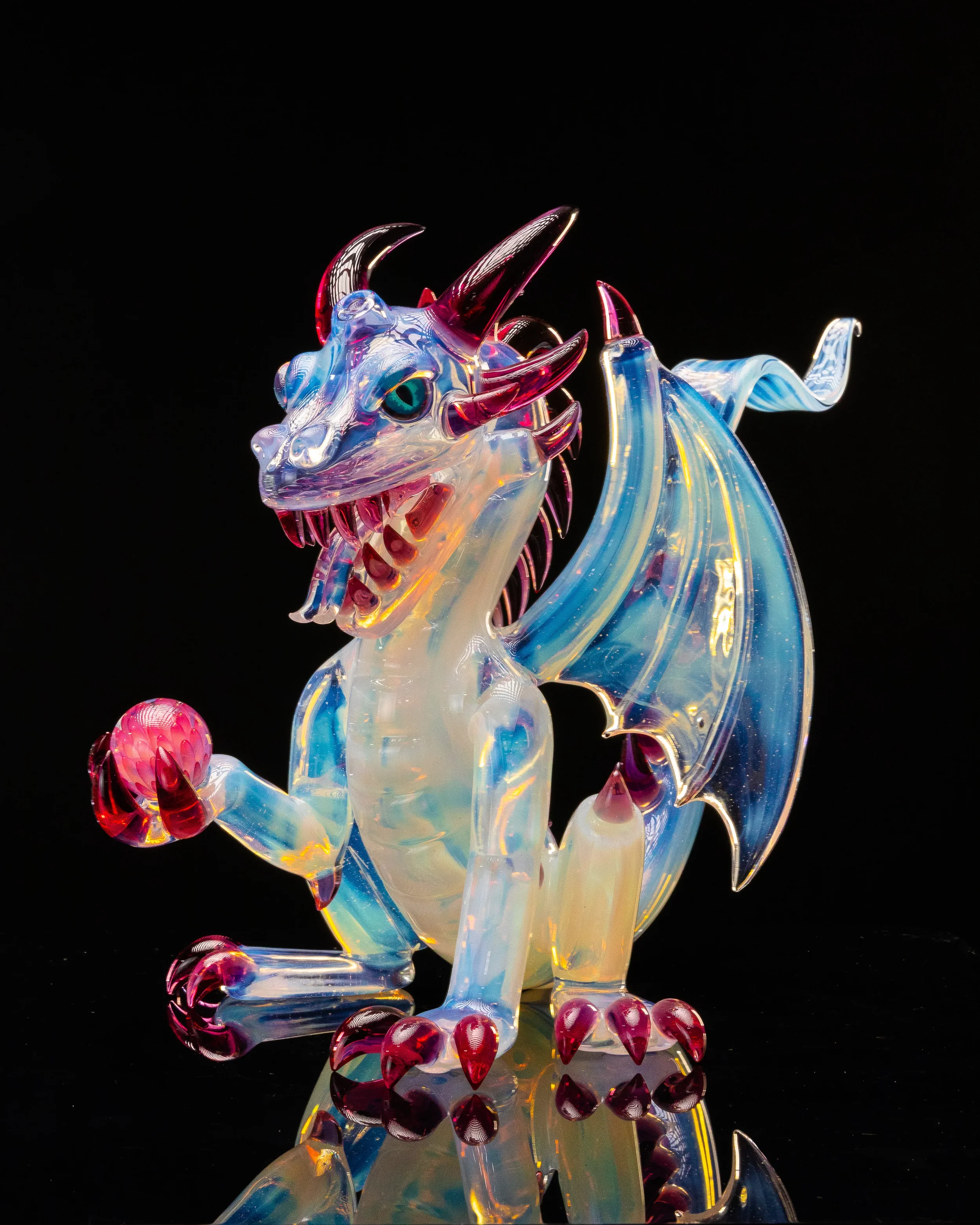 Colorful glass dragon sculpture with a blue eye, holding a pink orb, against a black background.