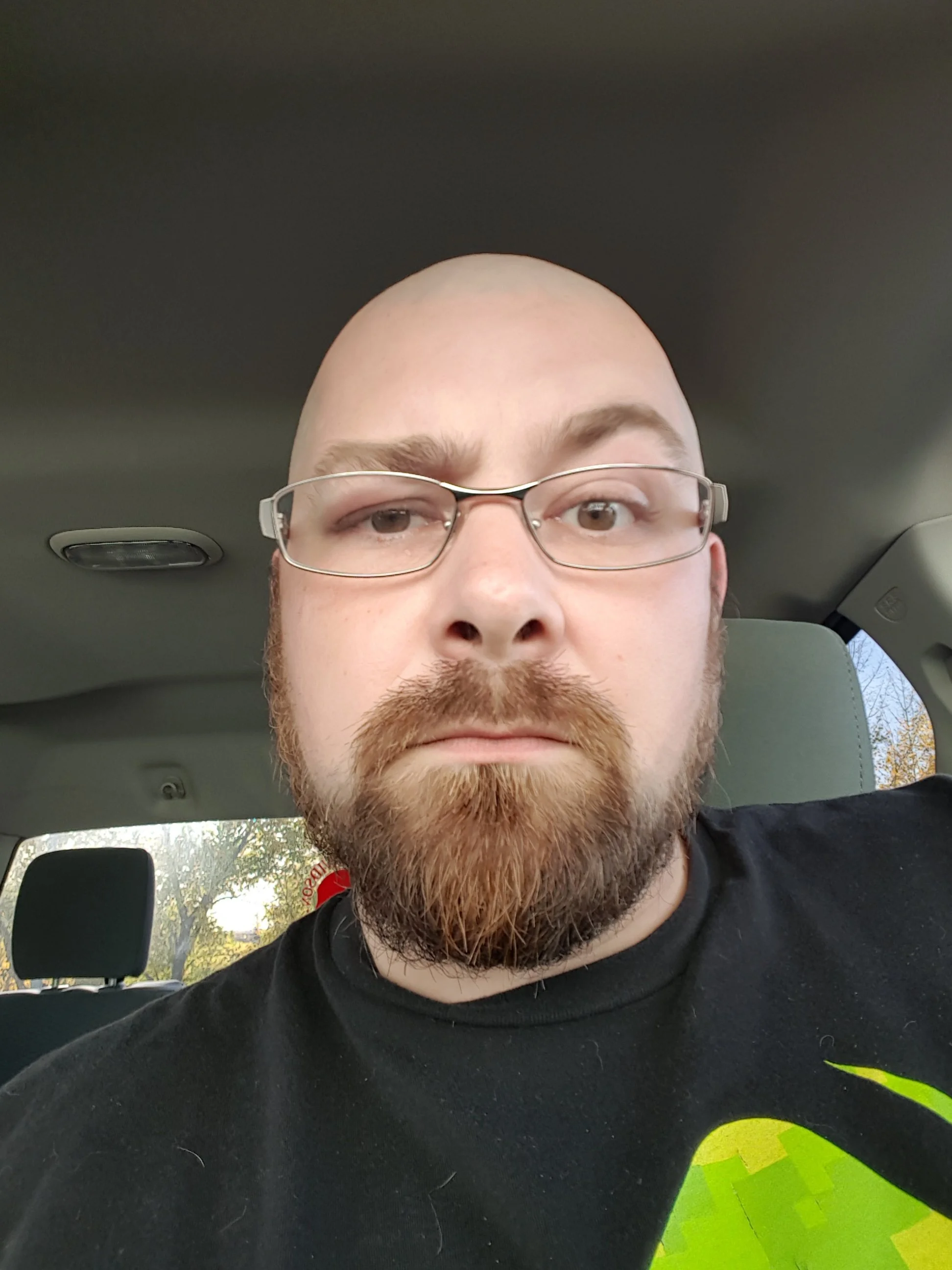 A man with glasses and a beard taking a selfie inside a vehicle.
