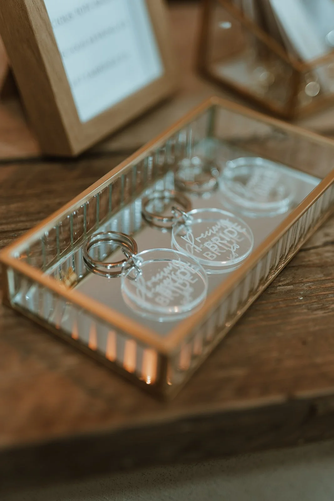 Clear acrylic keychains with engraved script reading 'Trevino BRIDE' and rings attached, placed inside a mirrored, rectangular display container.