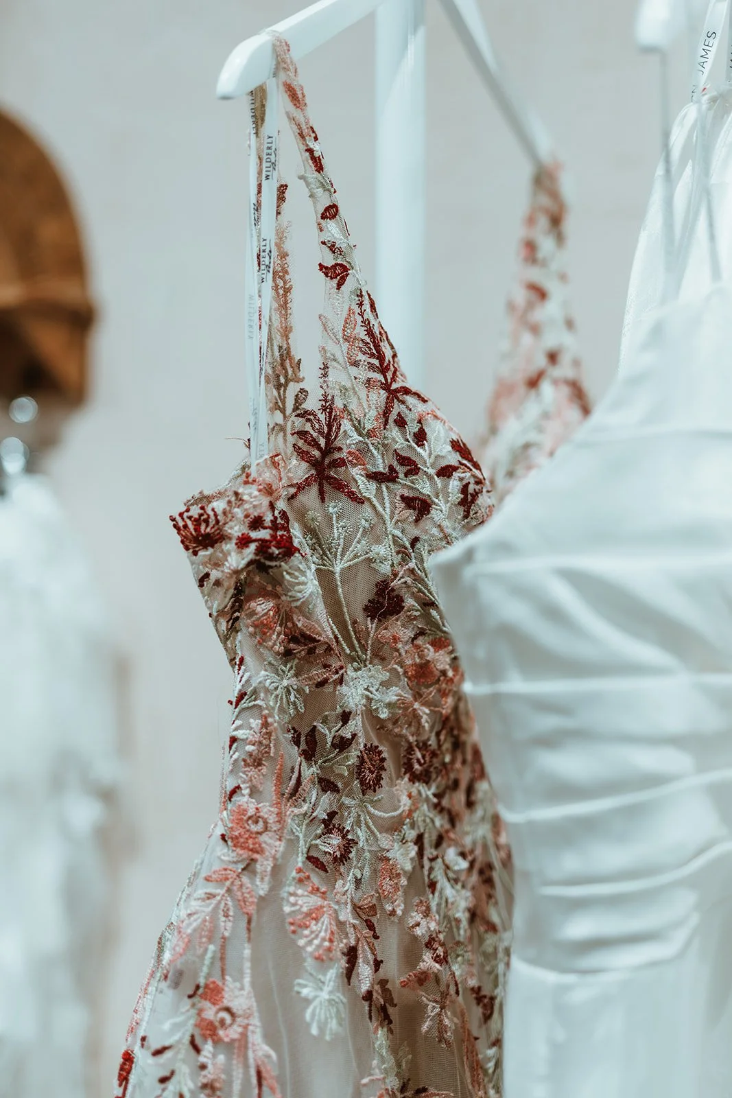 Close-up of floral embroidered beige and rust-colored dress hanging on a white hanger.