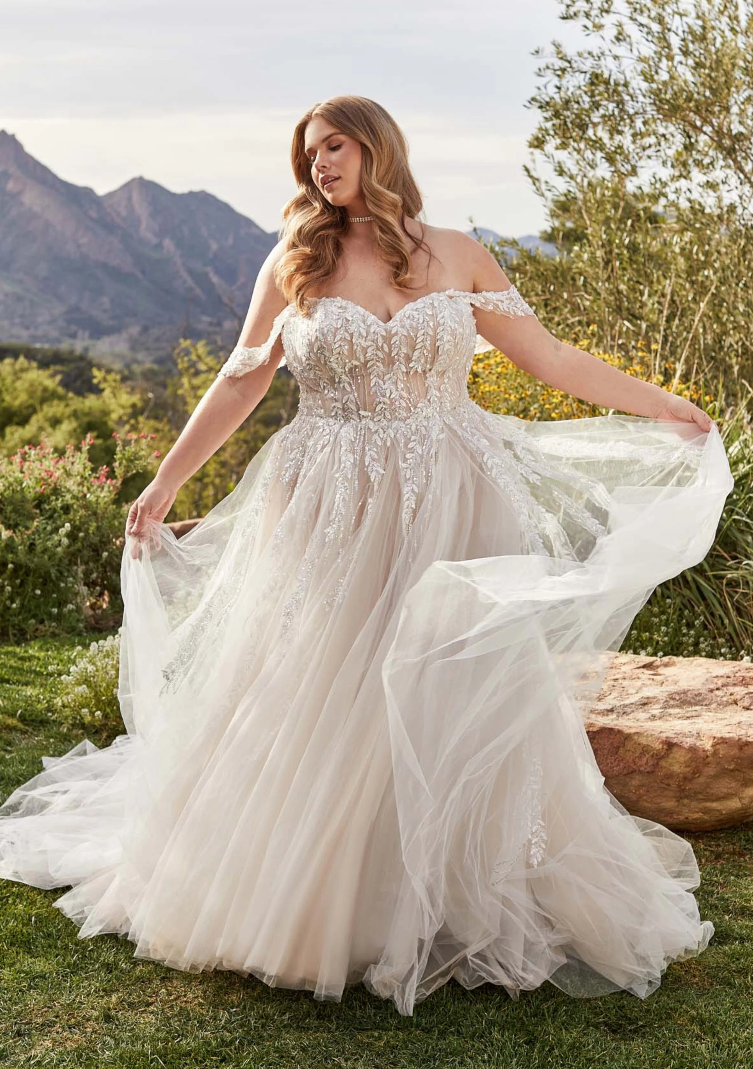 A woman in a wedding dress standing outdoors with mountains in the background.